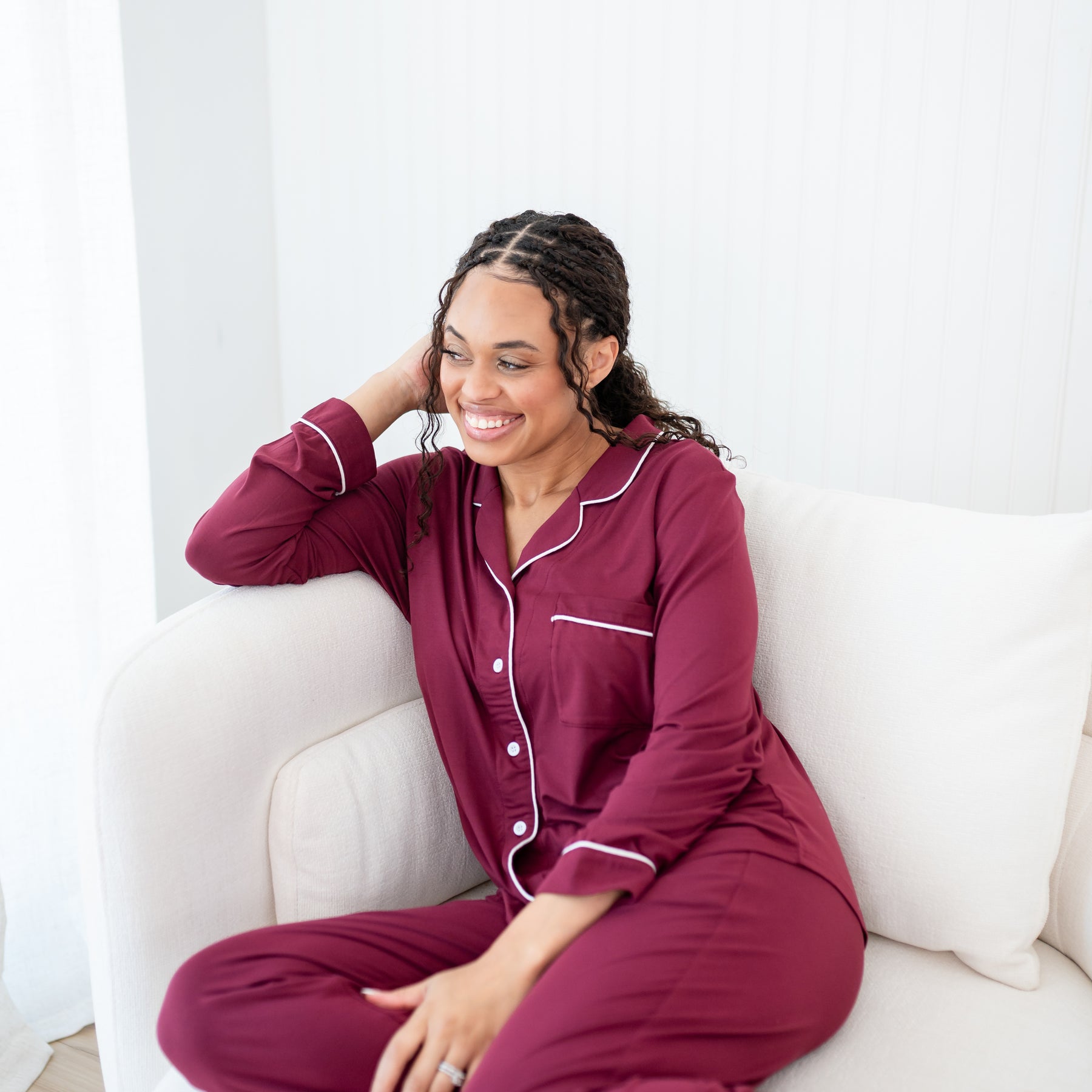 Smiling model sitting on a chair wearing the Long-Sleeved Women's Pajama Set in Burgundy with Cloud Trim