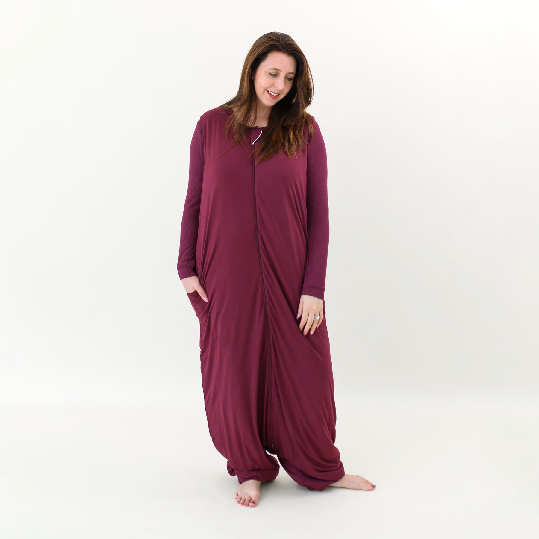 Smiling female standing looking at the ground with one hand in the pocket of the Adult Sleep Bag Walker in Burgundy