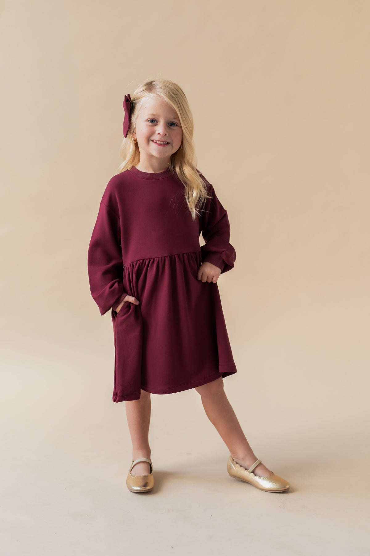 Girl wearing Long Sleeve Skater Dress in Burgundy color on a beige background