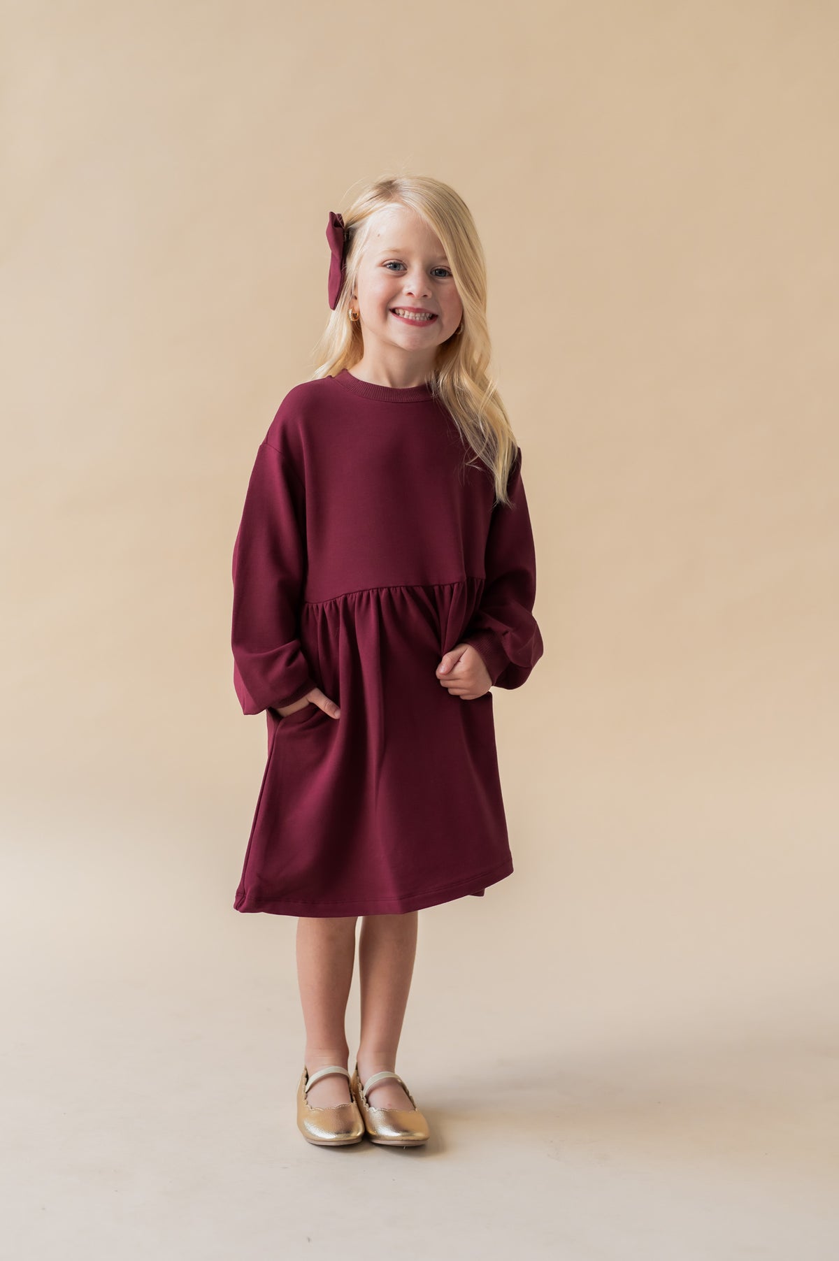 Girl smiling in Long Sleeve Skater Dress in Burgundy color on a beige background
