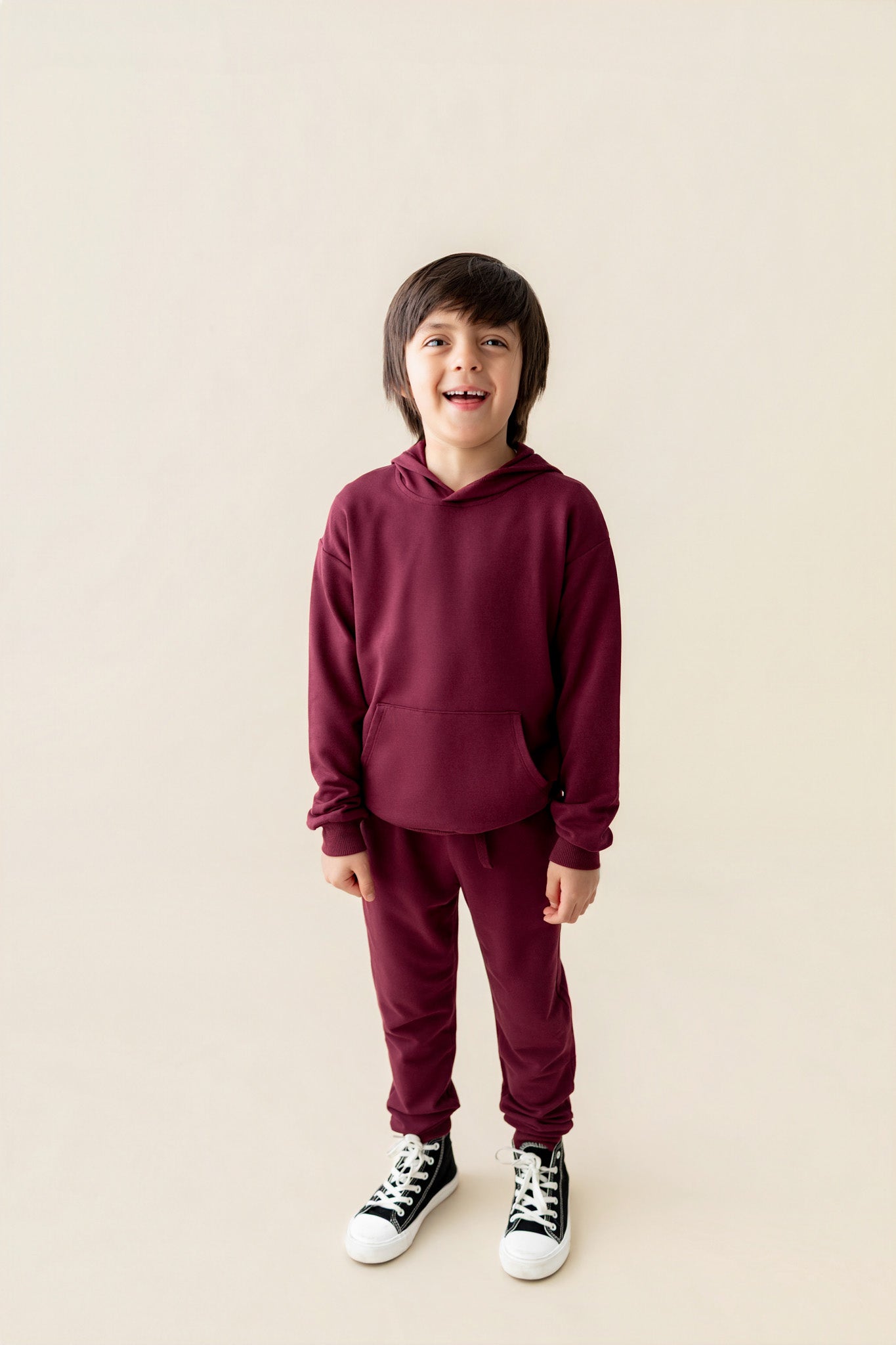Boy wearing Hoodie in Burgundy color and similar color pants on a beige background