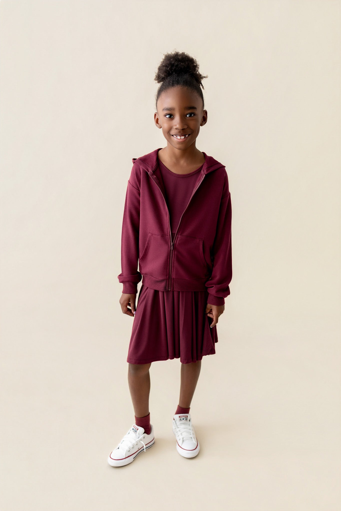 Girl wearing Zip-Up Hoodie in Burgundy color over long sleeve skater dress in burgundy on a beige background