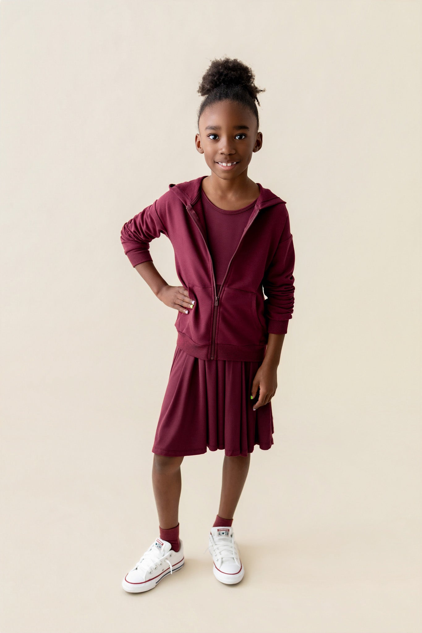 Girl wearing Zip-Up Hoodie in Burgundy color over long sleeve skater dress in burgundy and white shoes on a beige background