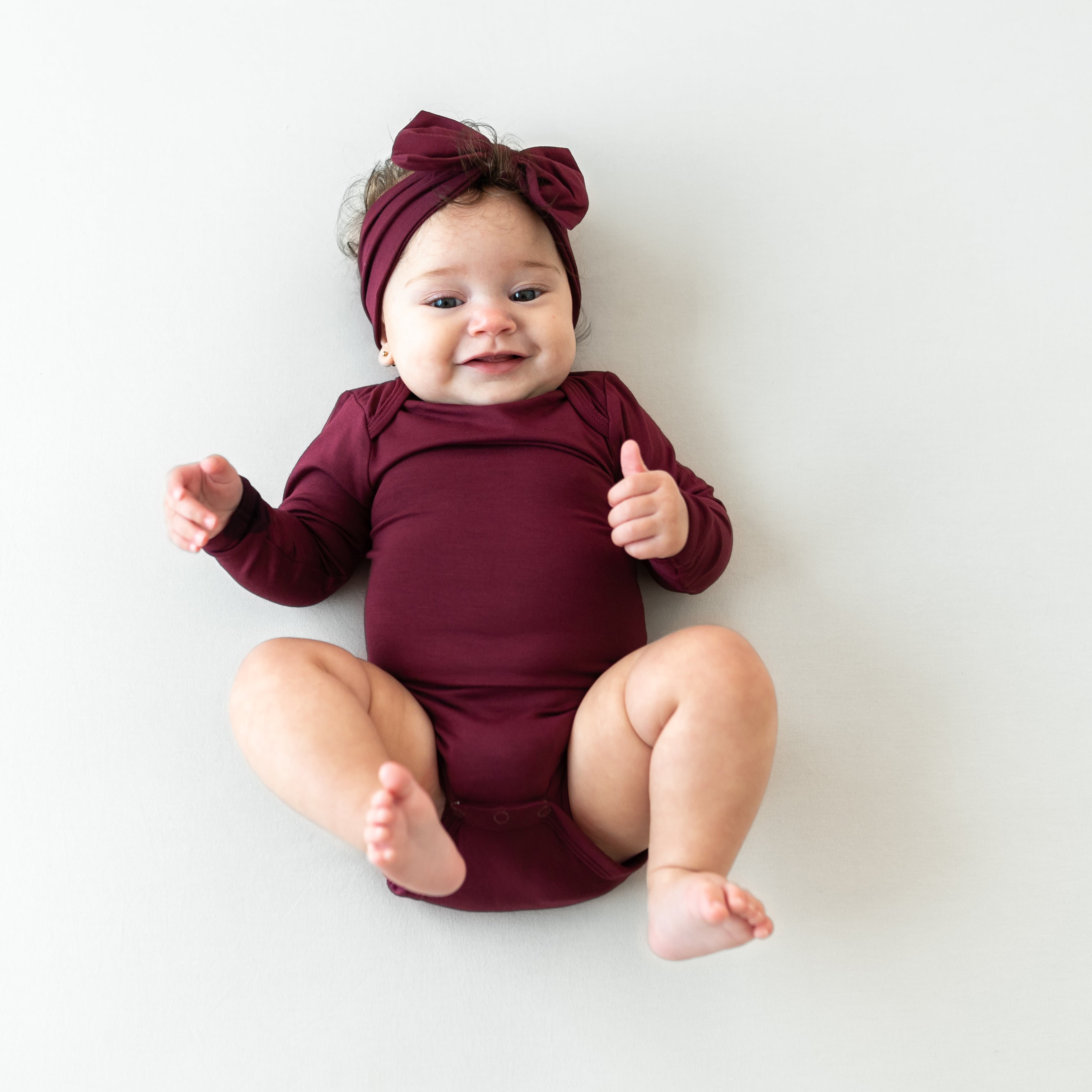 smiling infant wearing the Long Sleeve Bodysuit in Burgundy with matching long sleeve bodysuit