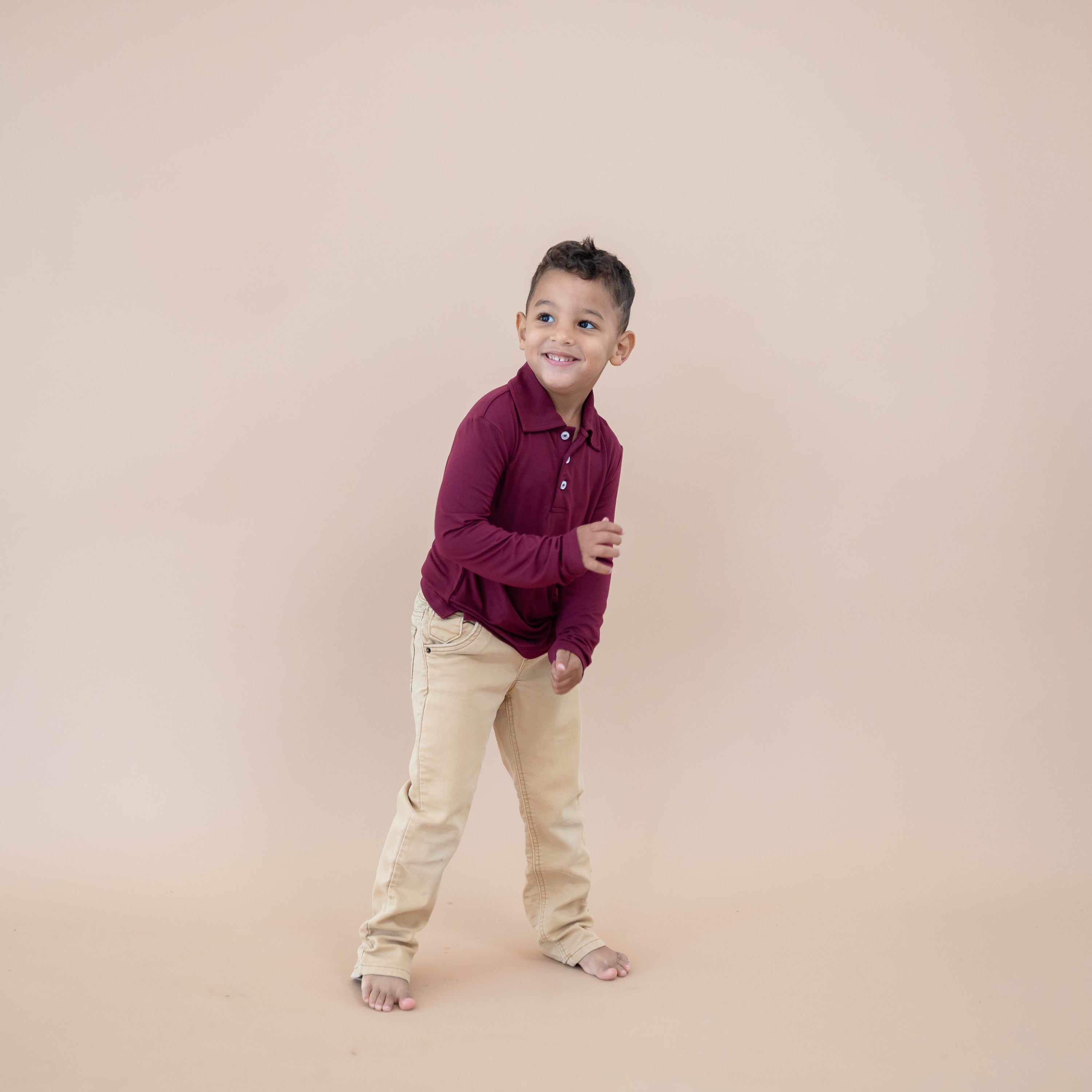 Boy model wearing the Toddler Long Sleeve Polo in Burgundy paired with khaki pants