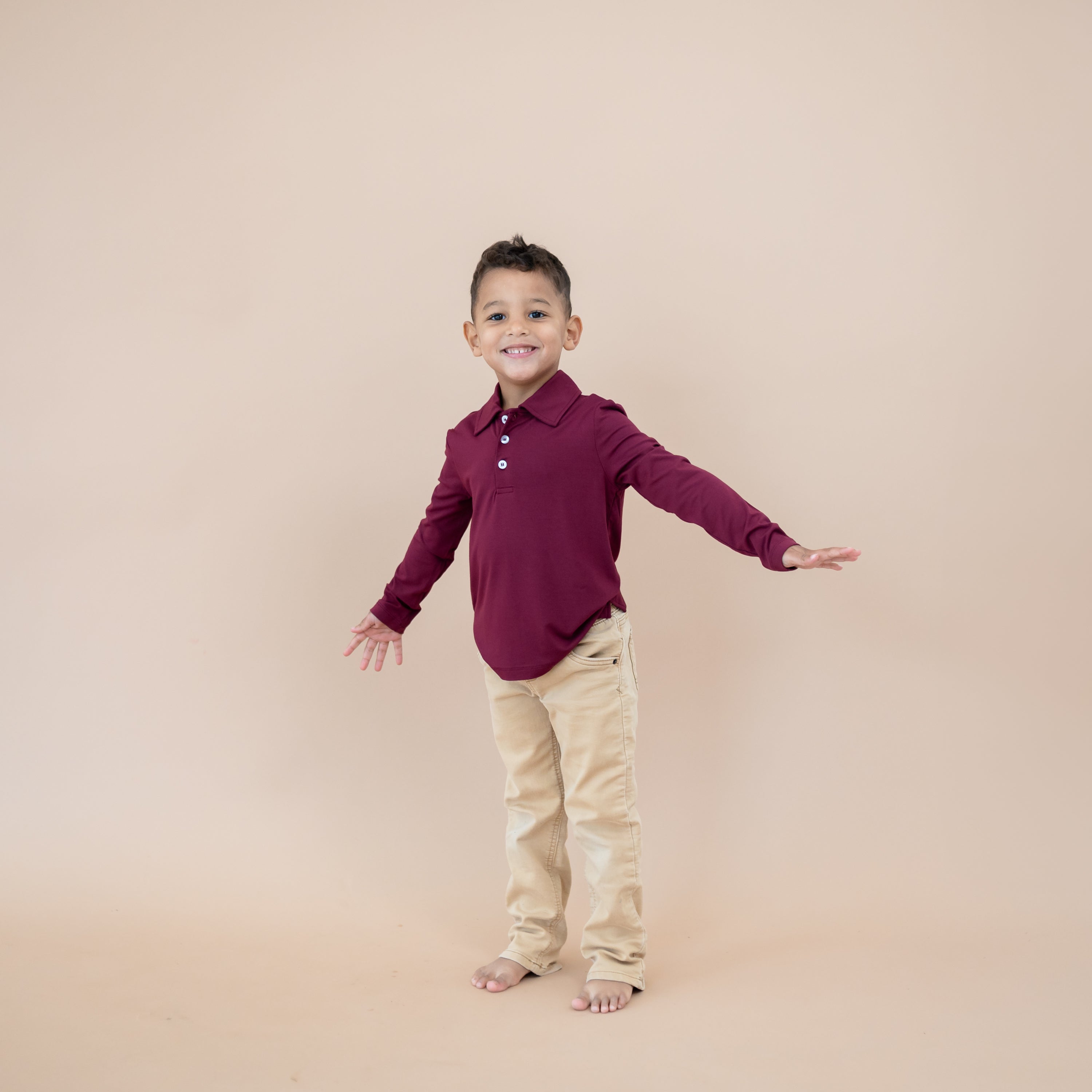 Young boy modeling the Toddler Long Sleeve Polo in Burgundy paired with khaki pants