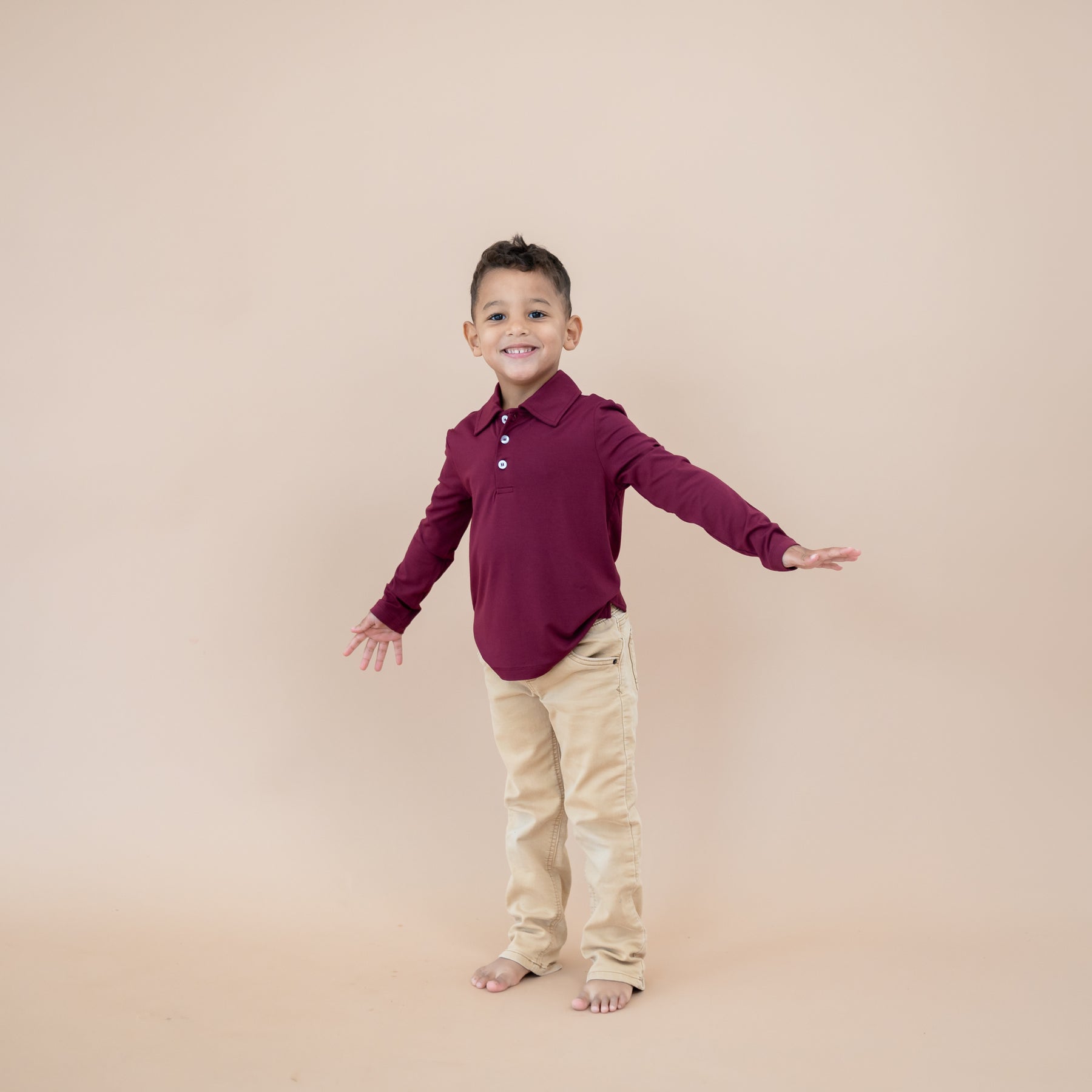 Young boy modeling the Toddler Long Sleeve Polo in Burgundy paired with khaki pants