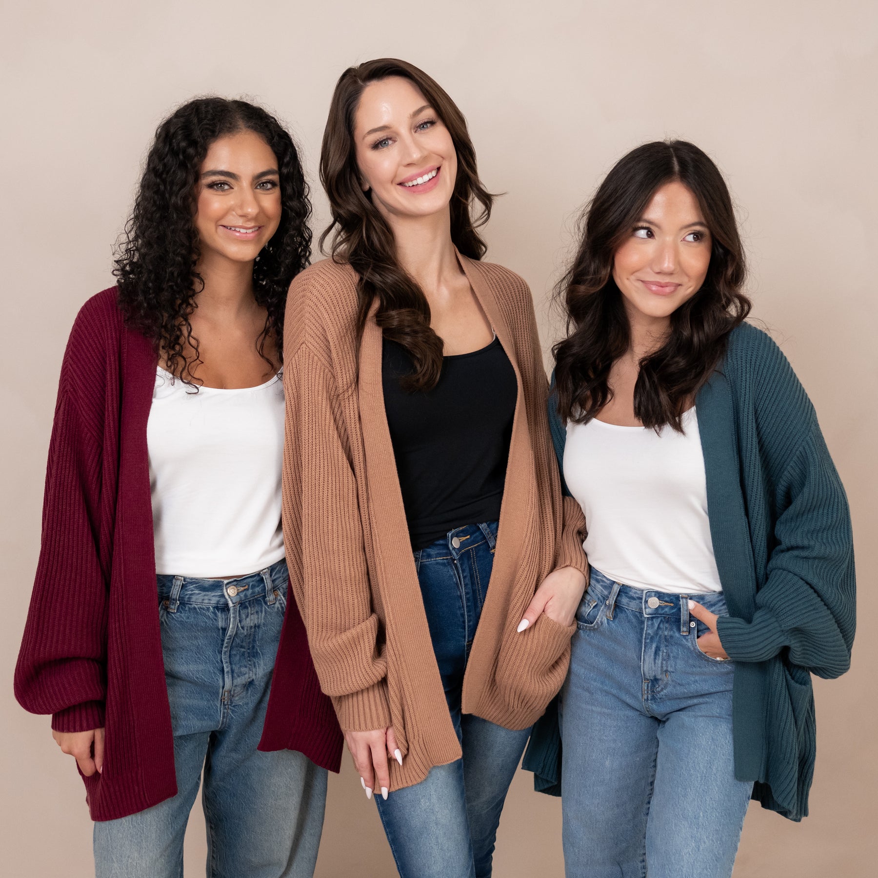 Three female models standing side by side wearing the Chunky Knit Women's Oversized Cardigan in Latte, Atlantic and Burgundy