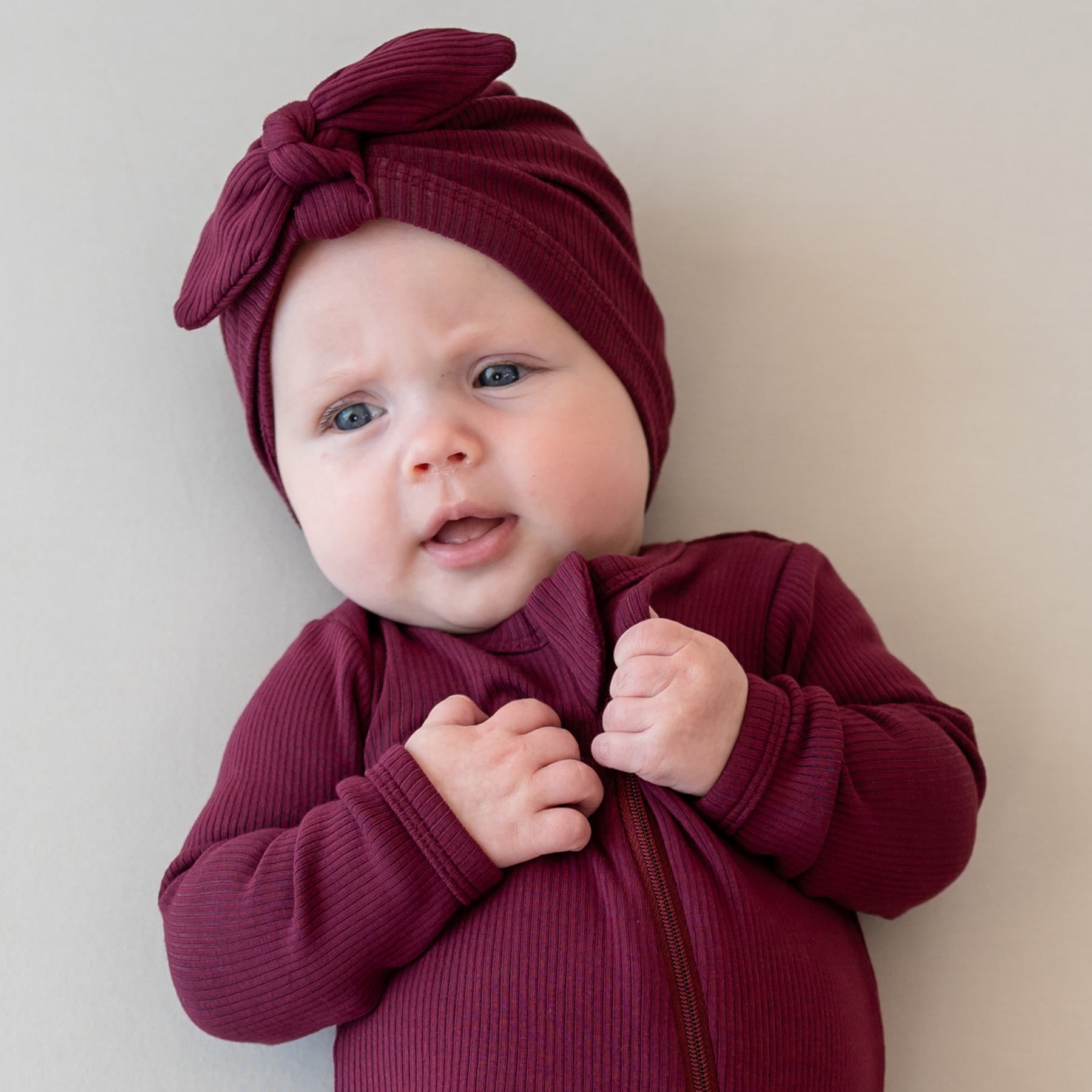 Infant wearing the Ribbed Headwrap in Burgundy looking off to the side wearing matching ribbed zipper romper
