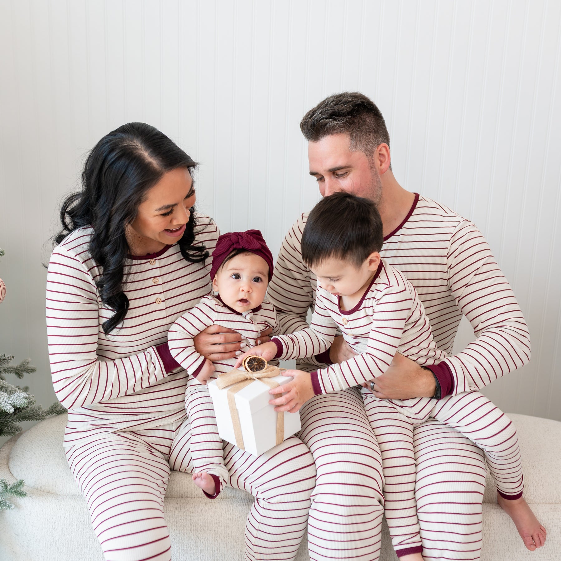 Family of four sitting on a cream ottoman matching in Burgundy Stripe items