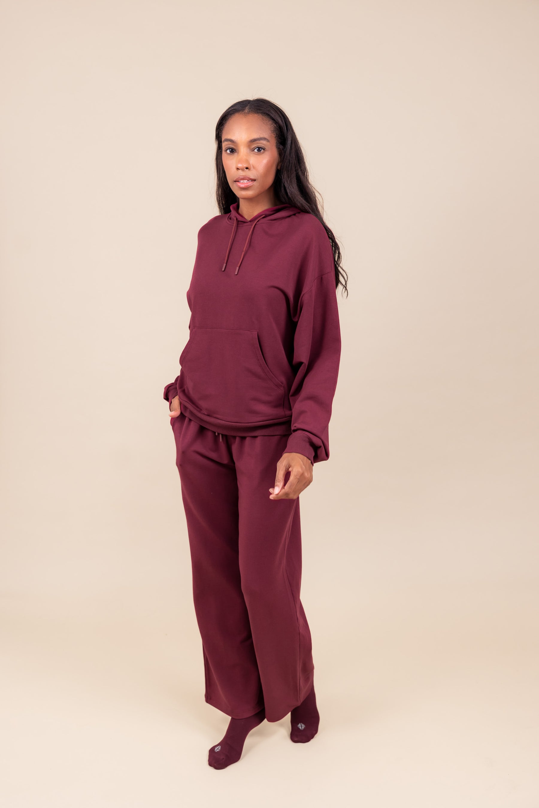 Woman wearing Women's Hoodie in Burgundy color over similar color women's sweatpants on a beige background