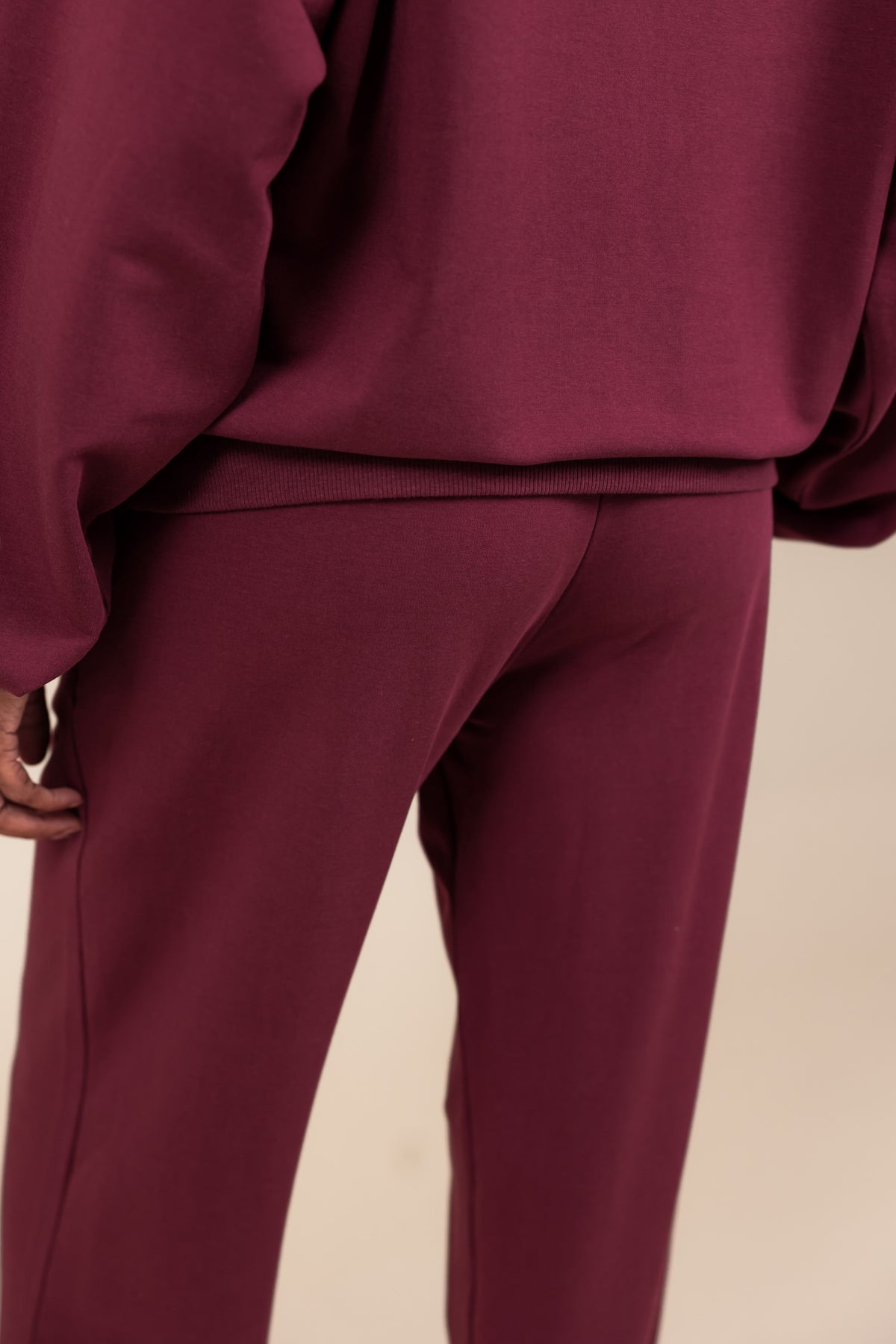 Back side of Modal wearing Women's Sweatpants in Burgundy color under similar color hoodie on a beige background