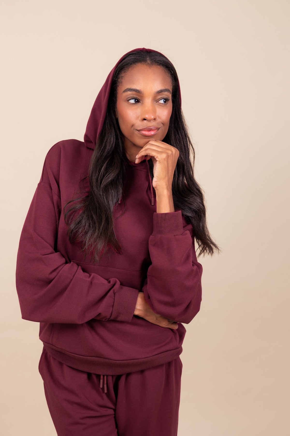Woman wearing Women's Hoodie in Burgundy color over similar color women's sweatpants on a beige background