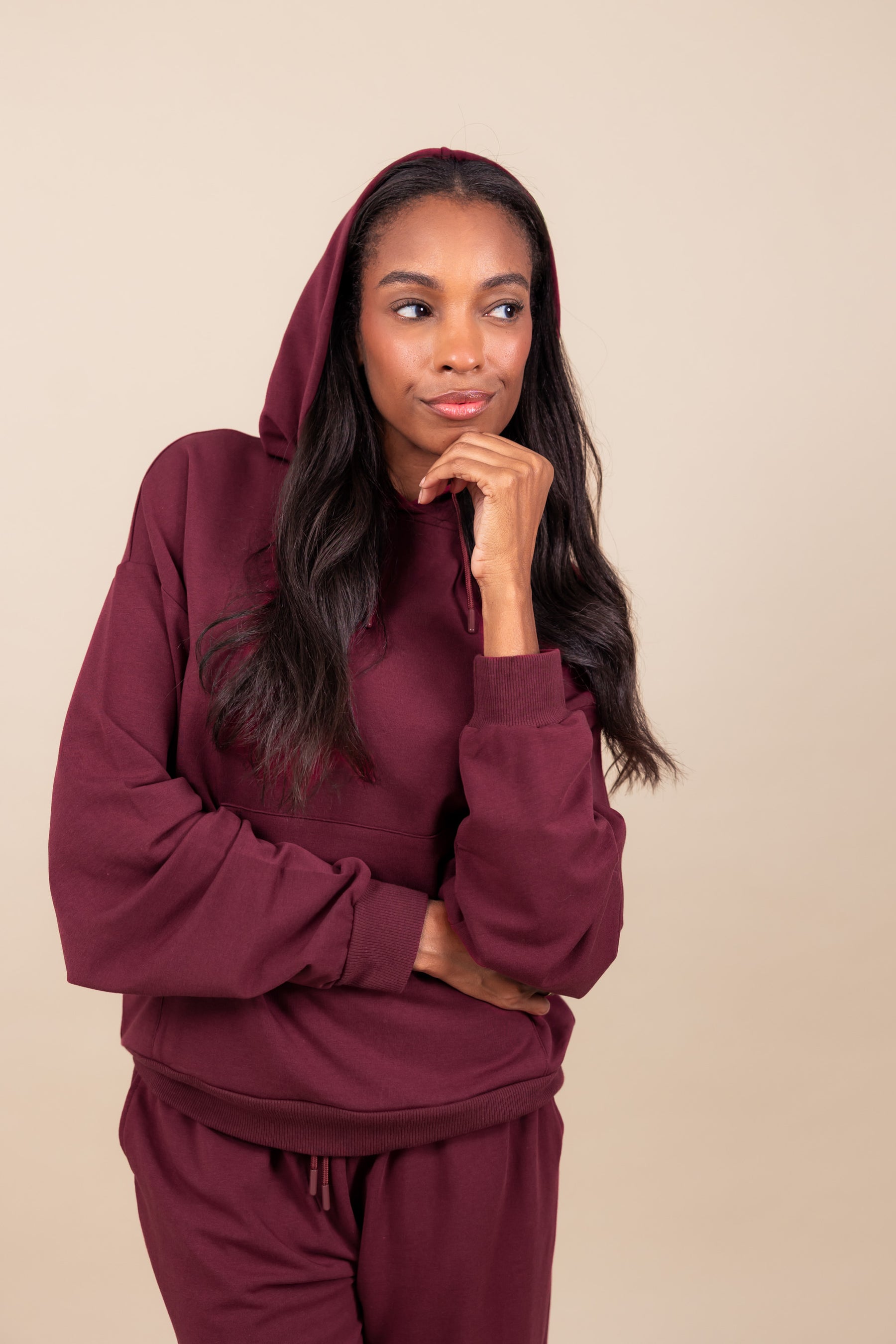 Woman wearing Women's Hoodie in Burgundy color over similar color women's sweatpants on a beige background