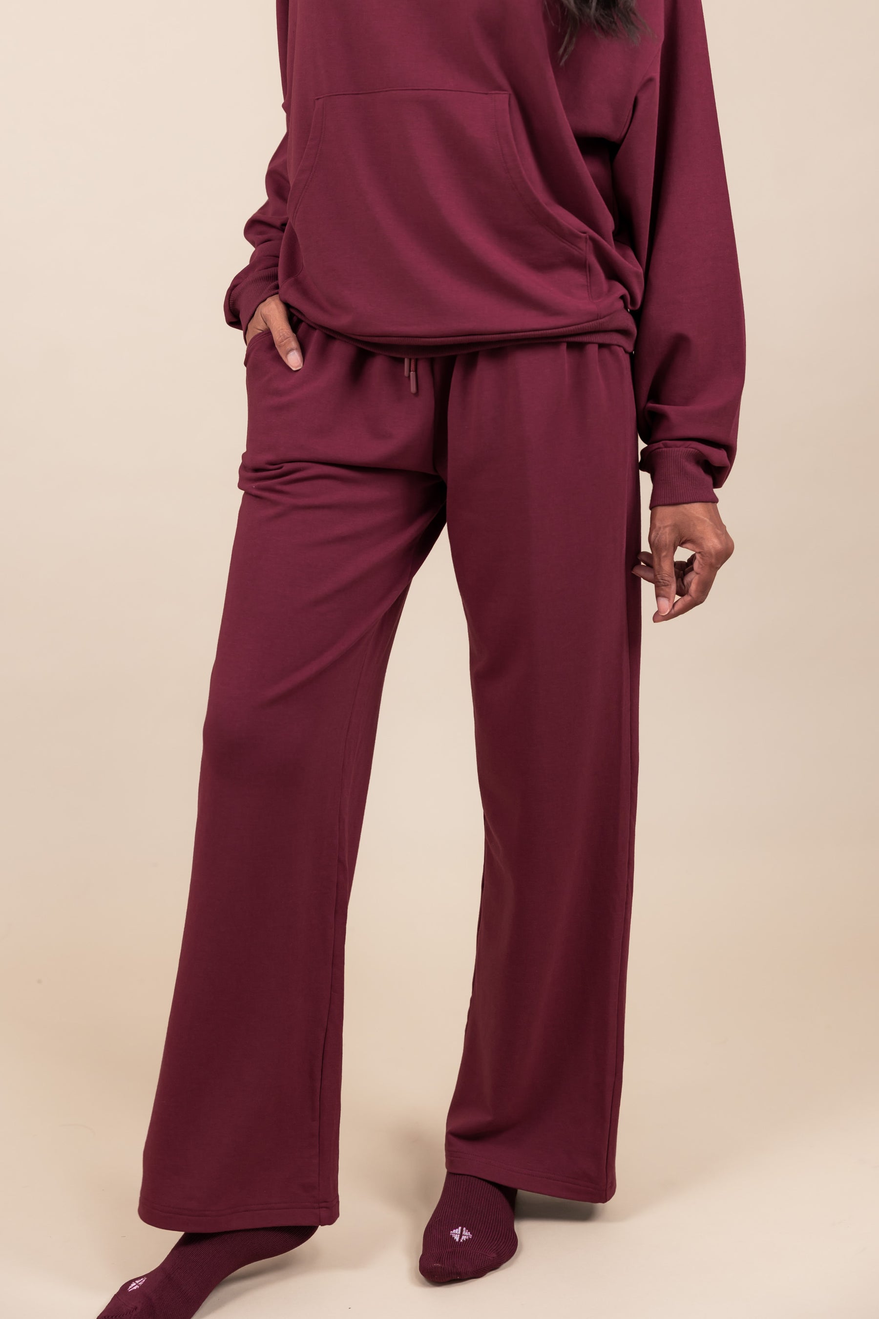 Modal wearing Women's Sweatpants in Burgundy color under similar color hoodie on a beige background