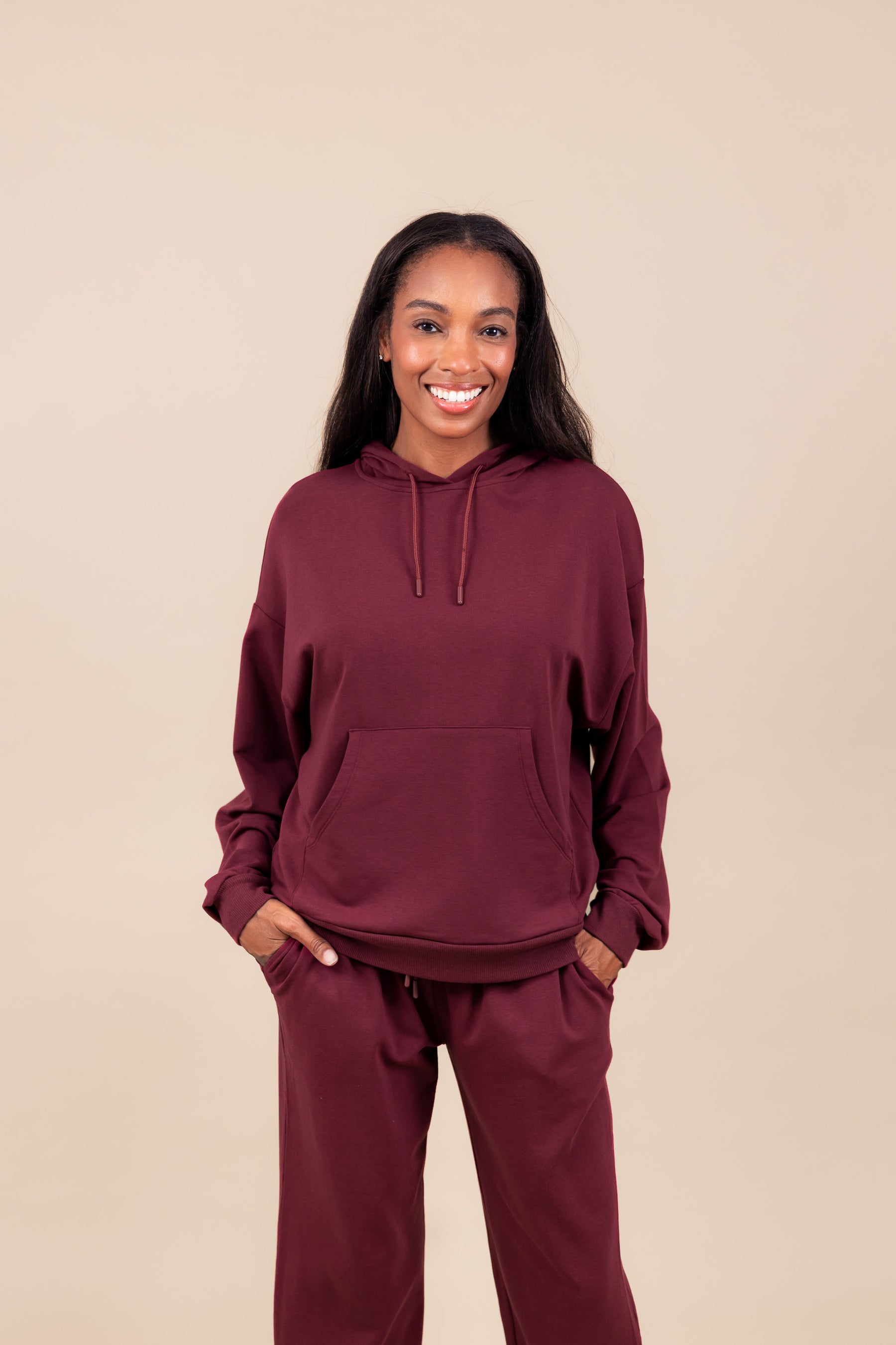Woman smiling in Women's Hoodie in Burgundy color over similar color women's sweatpants with pockets on a beige background