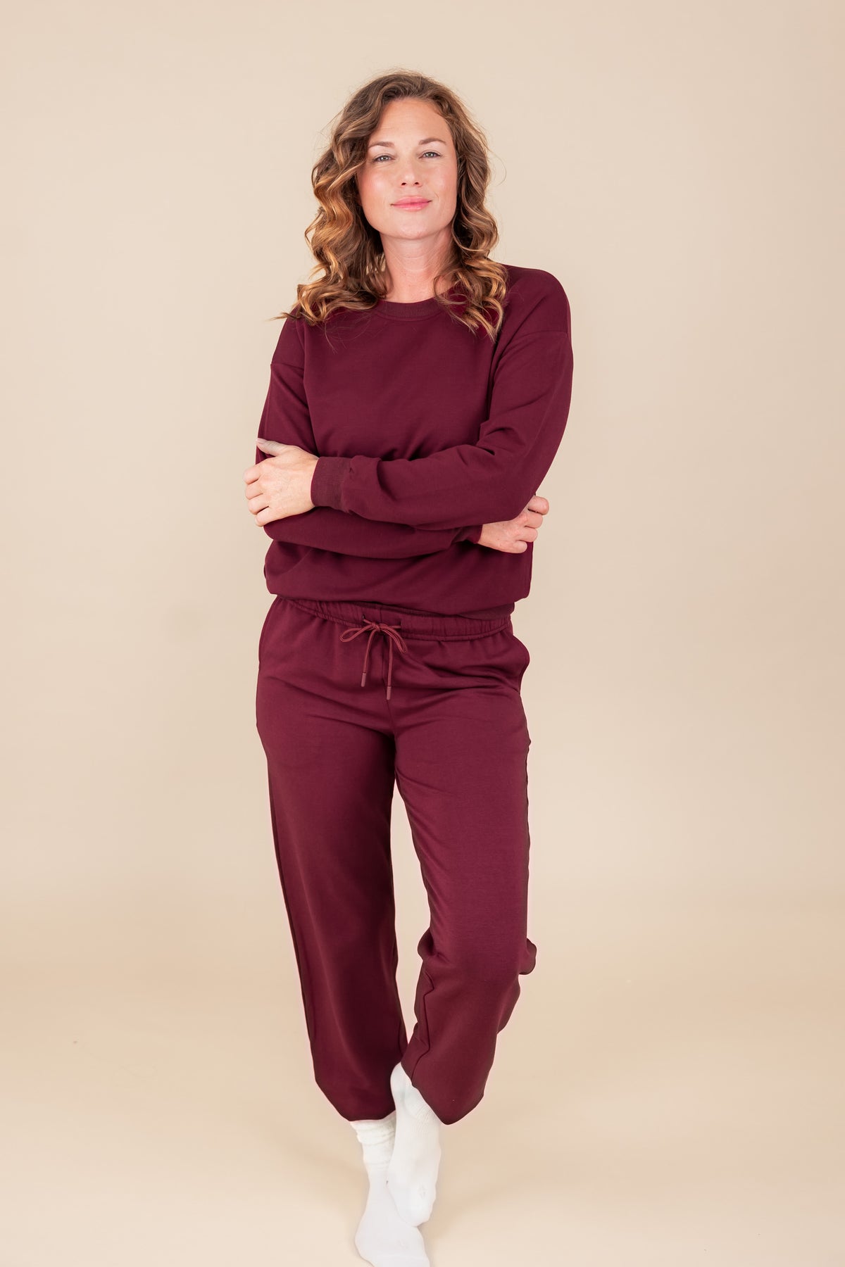 Woman smiling in Women's Jogger Pant in Burgundy color with crossed hands under similar color sweatshirt on a beige background