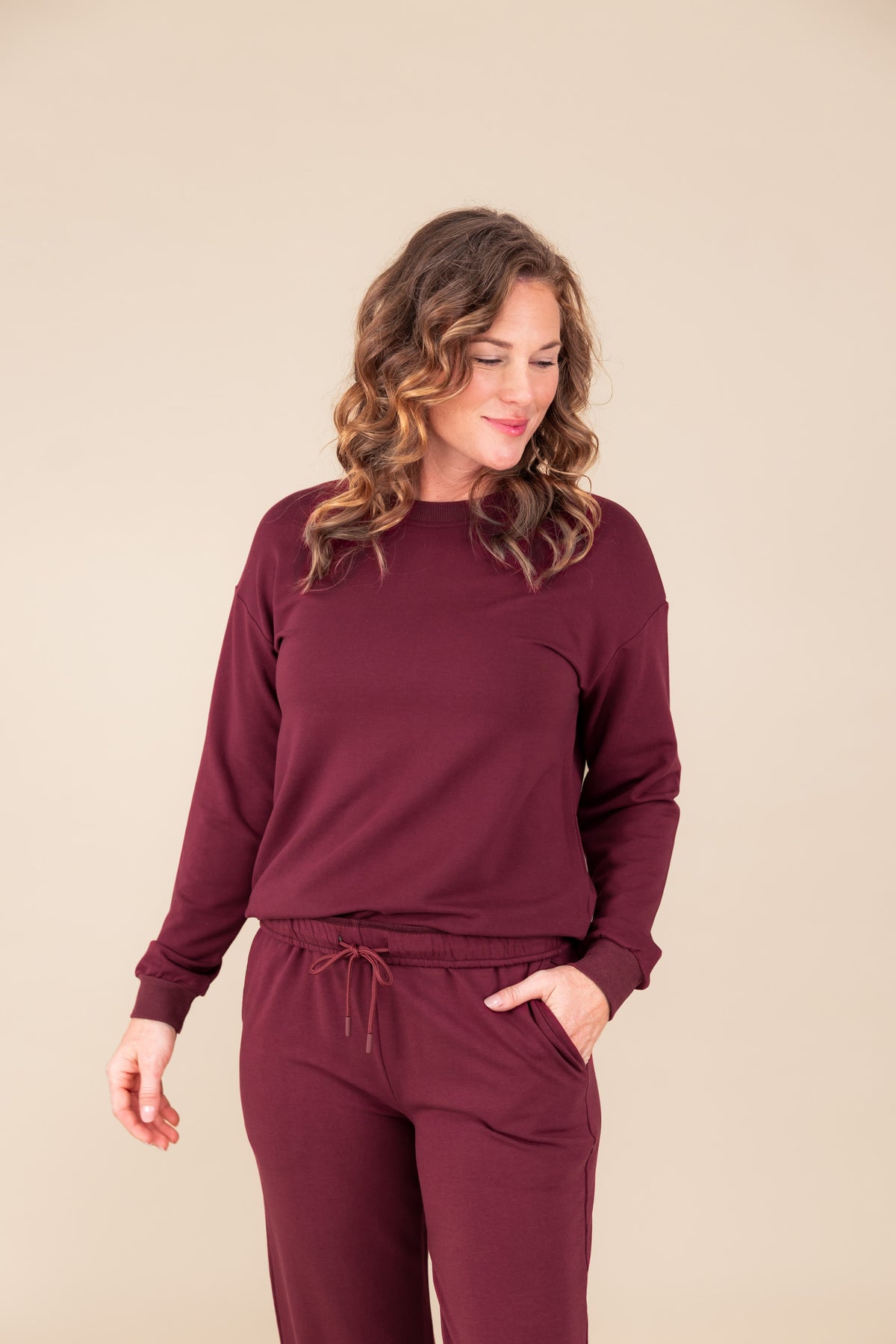 Woman wearing Women's Sweatshirt in Burgundy color over women's jogger pants in burgundy on a beige background