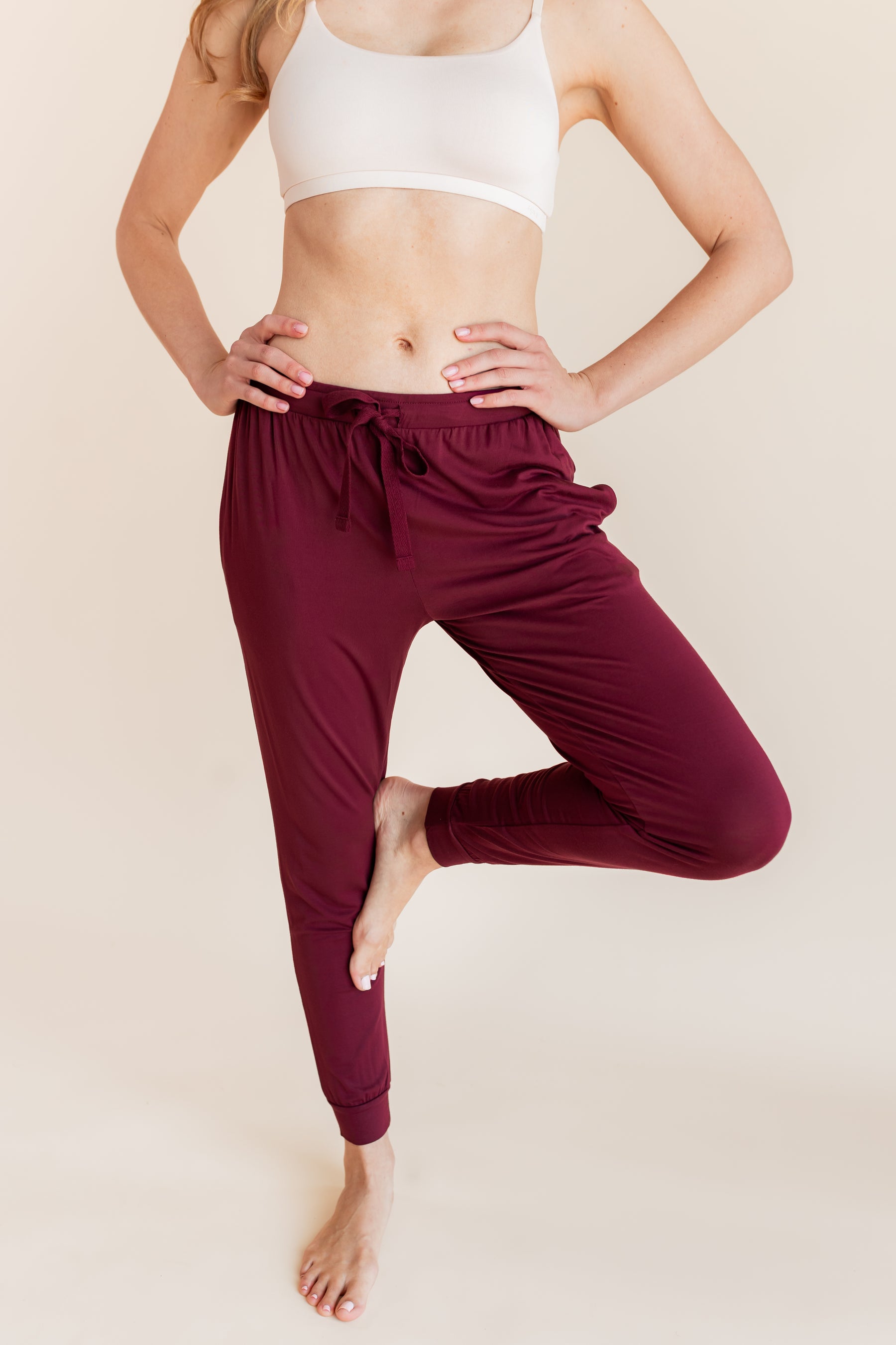 Model wearing Women's Jogger Pants in Burgundy under white bralette on a beige background