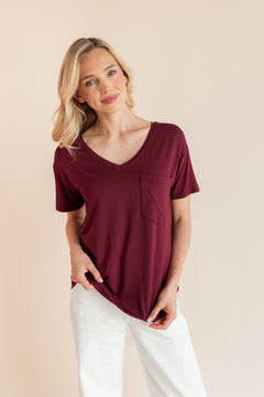 Model wearing Women's Oversized V-Neck Tee in Burgundy over white pants on a beige background