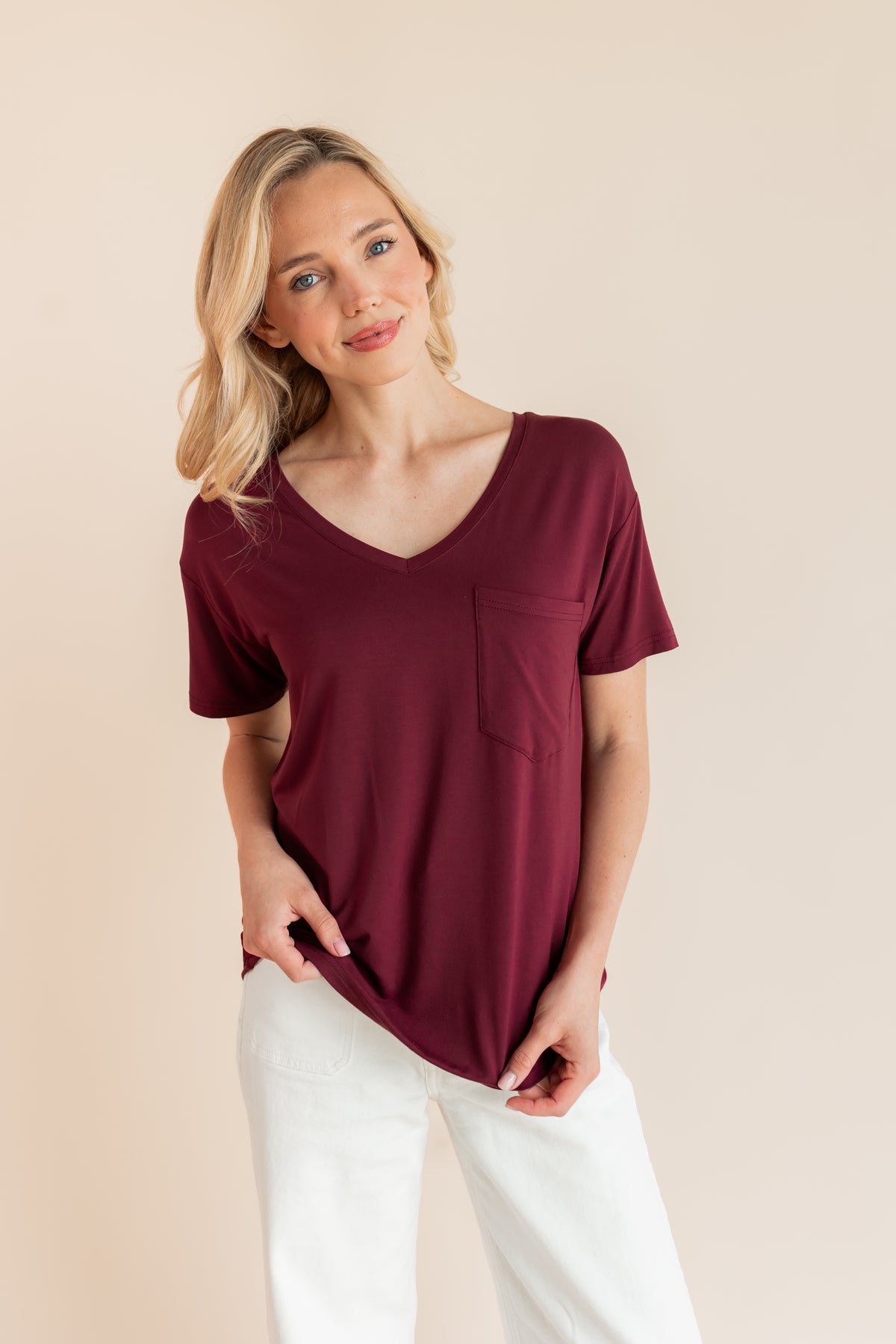 Model wearing Women's Oversized V-Neck Tee in Burgundy over white pants on a beige background