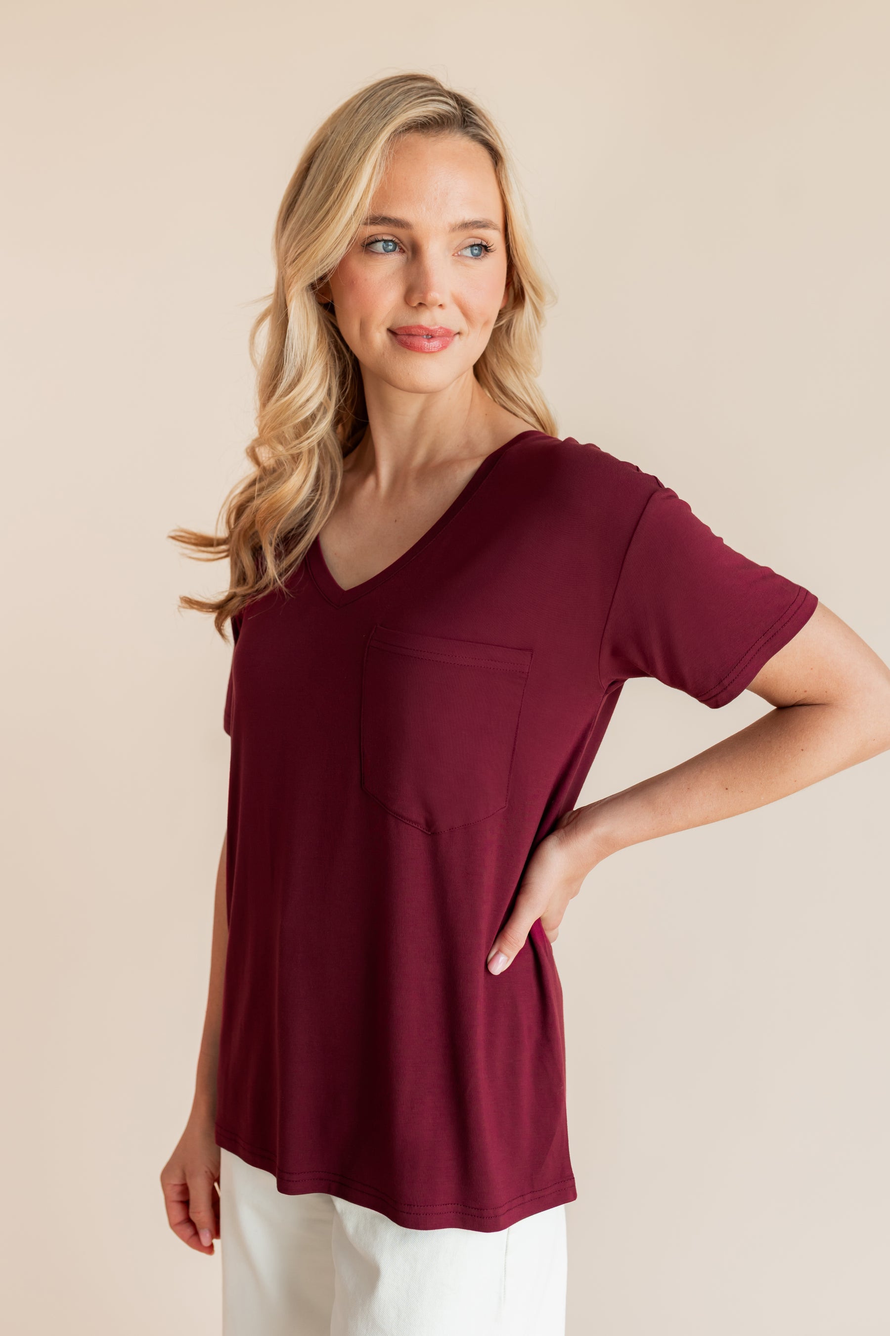 Model wearing Women's Oversized V-Neck Tee in Burgundy over white pants on a beige background