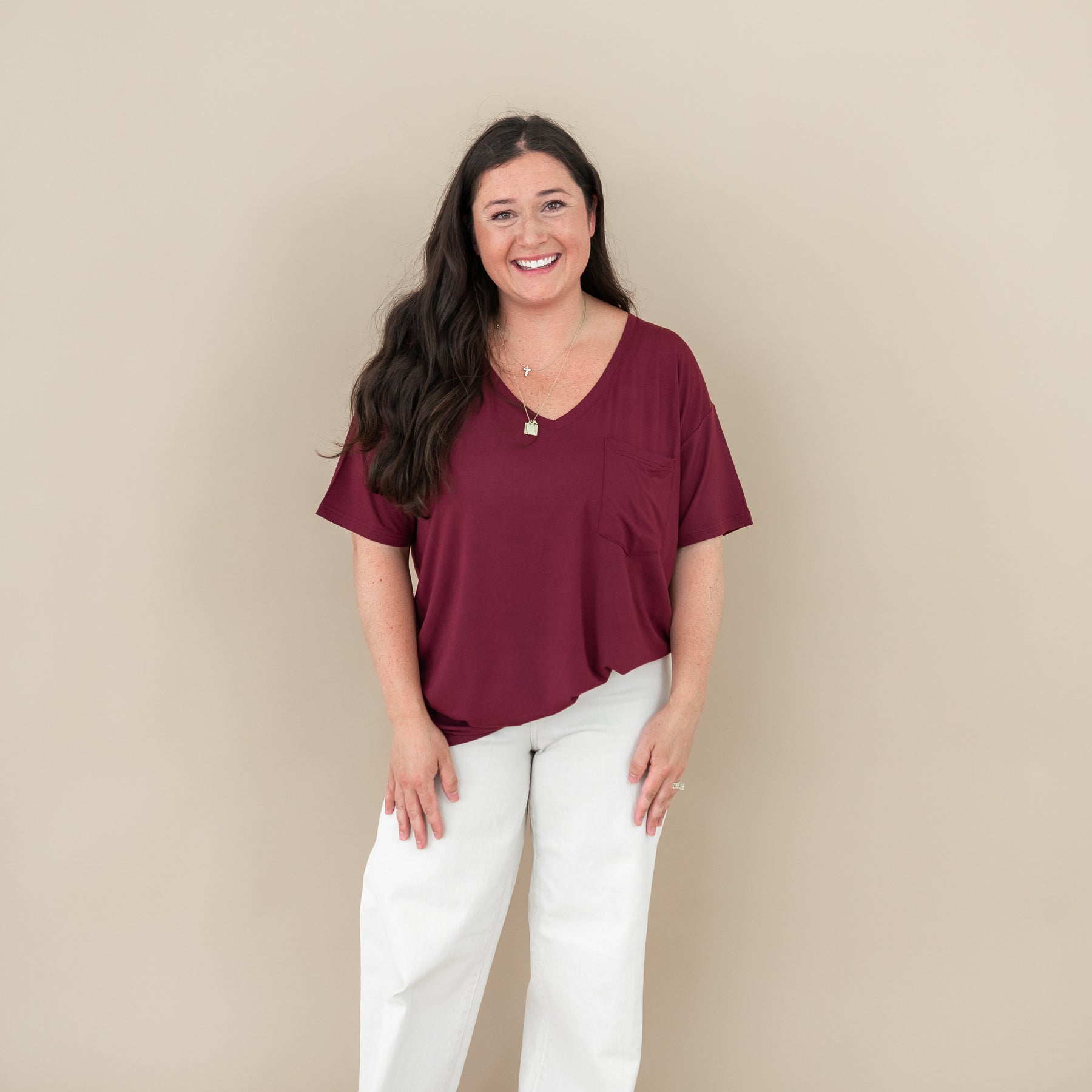 Smiling model standing with hands at her side wearing the Women’s Relaxed Fit V-Neck in Burgundy paired with cream pants