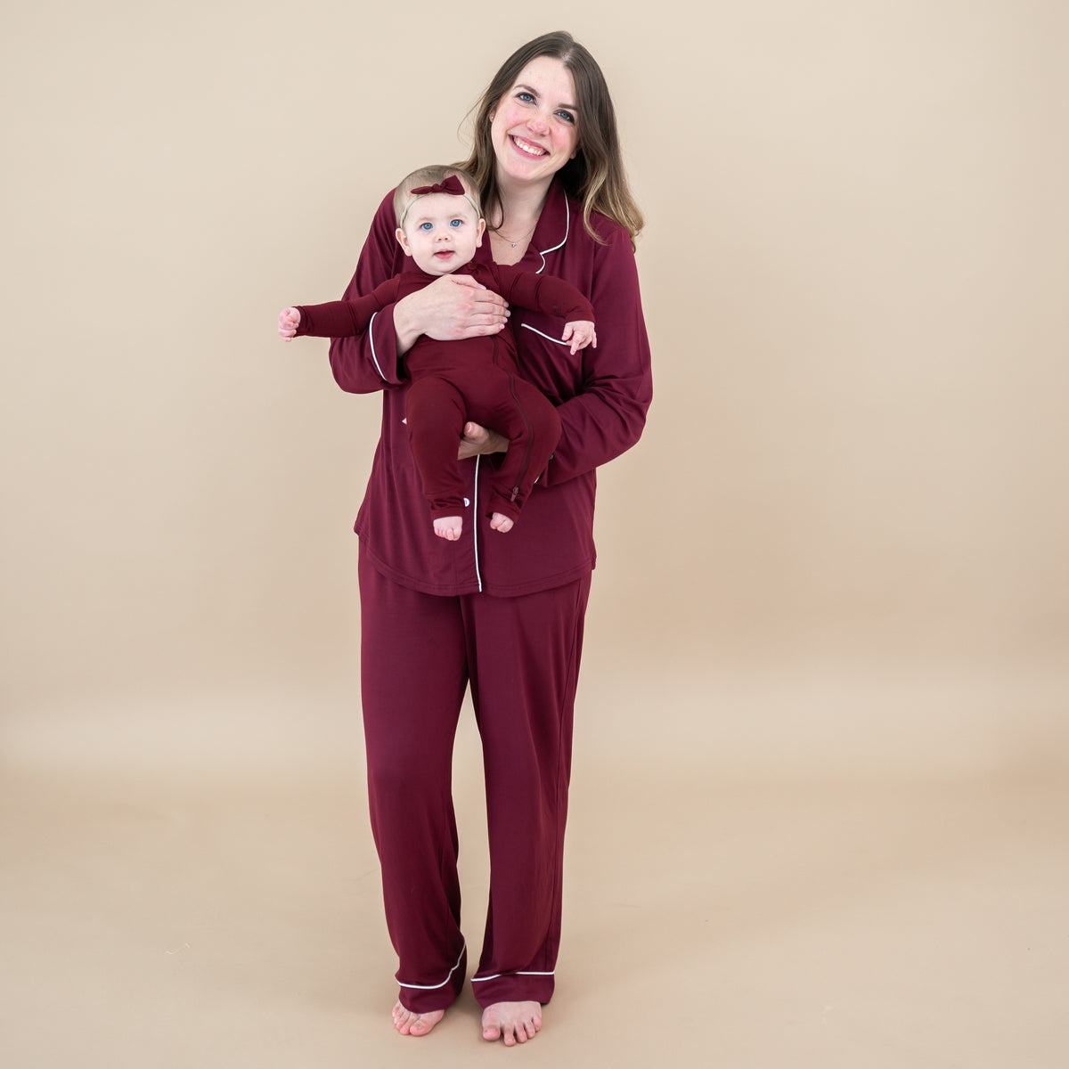 Mother and daughter matching wearing Burgundy. Pictured are the Long-Sleeved Women's Pajama Set in Burgundy with Cloud Trim, zippered romper and tiny nylon bow