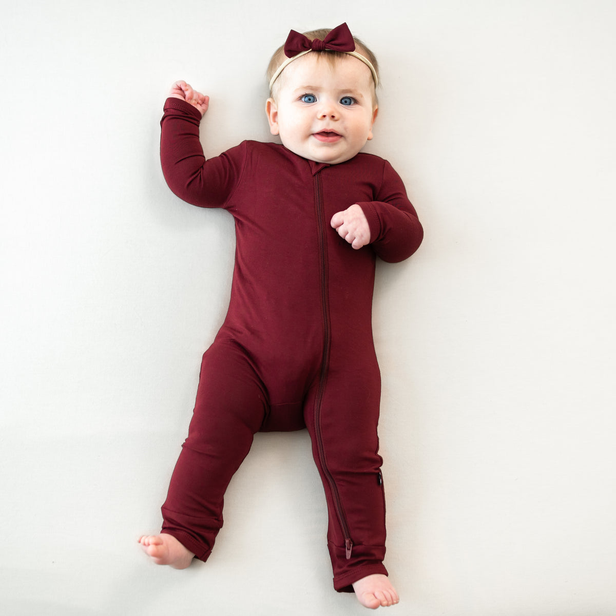 Infant model wearing the Zippered Romper in Burgundy with matching tiny nylon bow