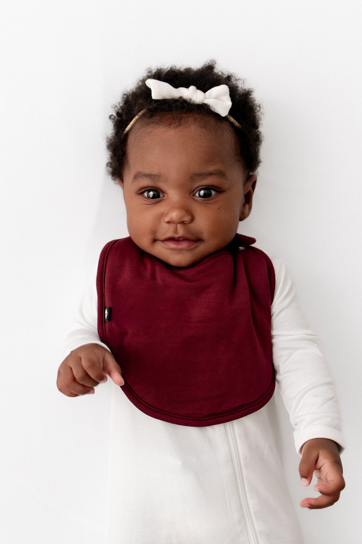 Infant wearing the Cushy Bib in Burgundy overtop a Cloud Zippered footie