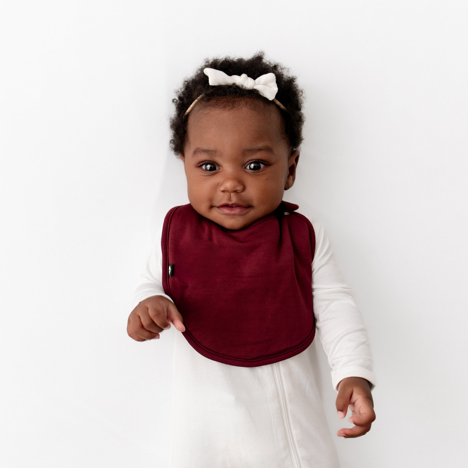 Infant wearing the Cushy Bib in Burgundy overtop a Cloud Zippered footie