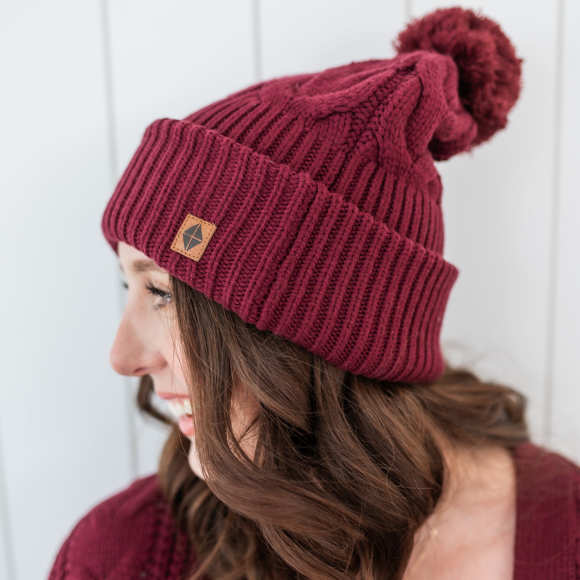 Close up of the Cable Knit Adult Pom Beanie in Burgundy shown on a female model