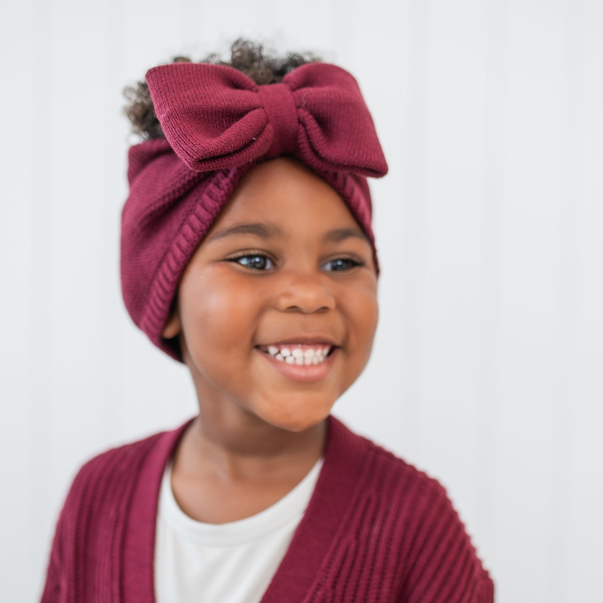 Smiling young girl modeling the Chunky Knit Bow Headband in Burgundy