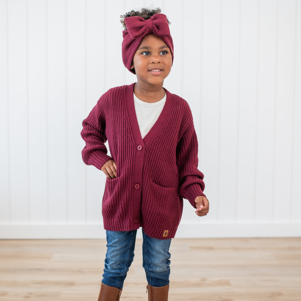 Young girl wearing the Chunky Knit Oversized Cardigan in Burgundy paired with matching Chunky knit bow headband