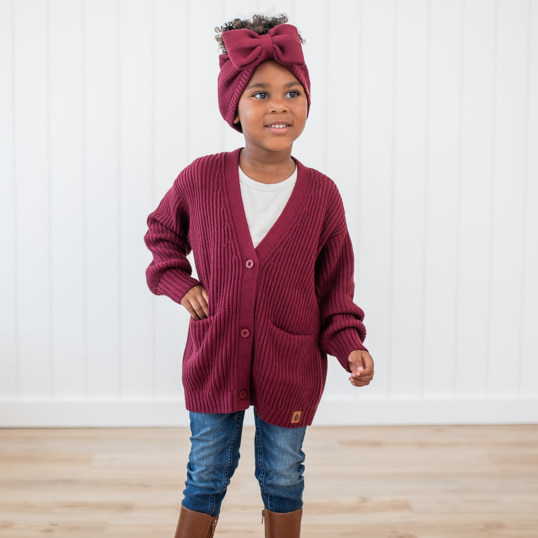 Young girl wearing the Chunky Knit Oversized Cardigan in Burgundy paired with matching Chunky knit bow headband