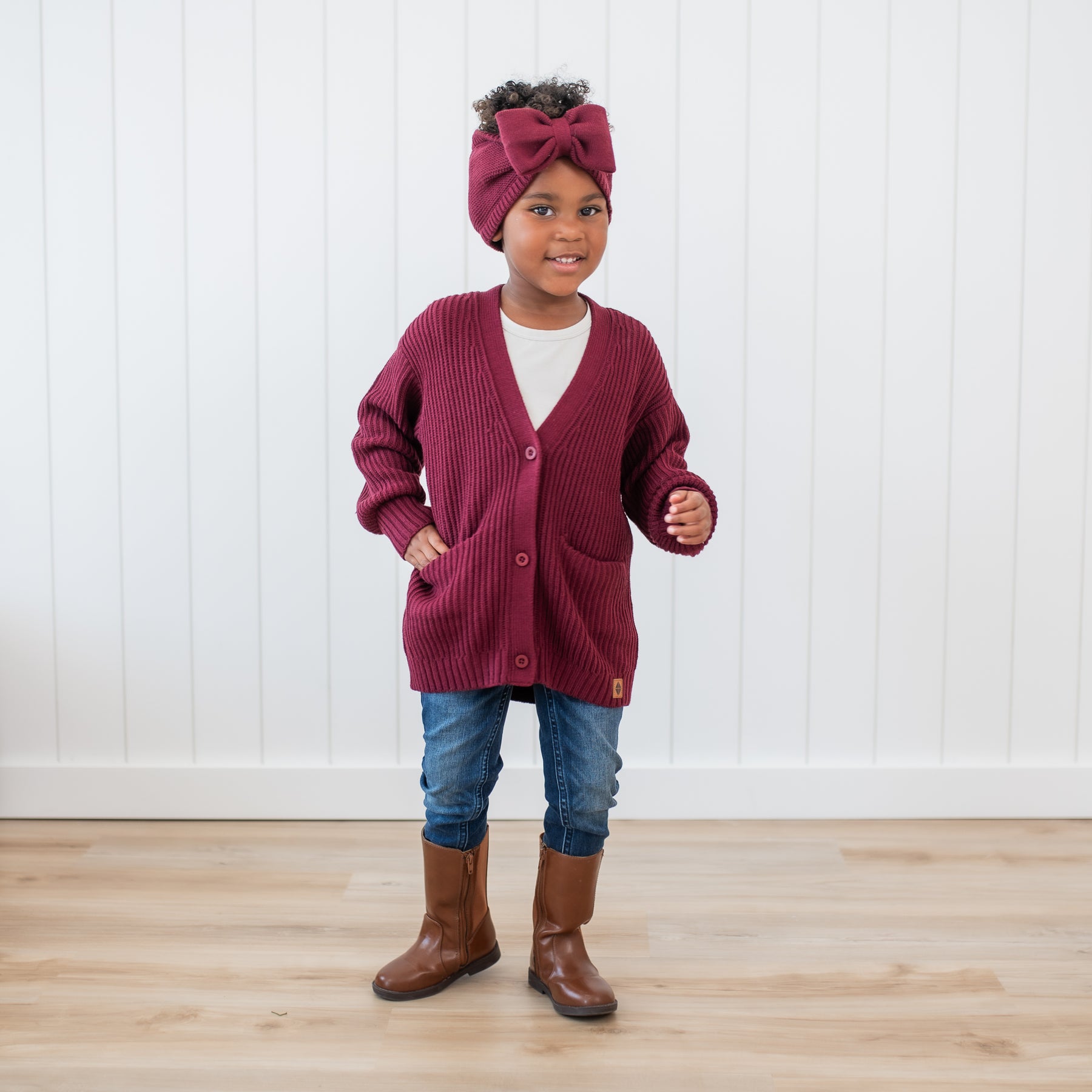 Young girl wearing the Chunky Knit Oversized Cardigan in Burgundy paired with medium wash jeans and brown boots