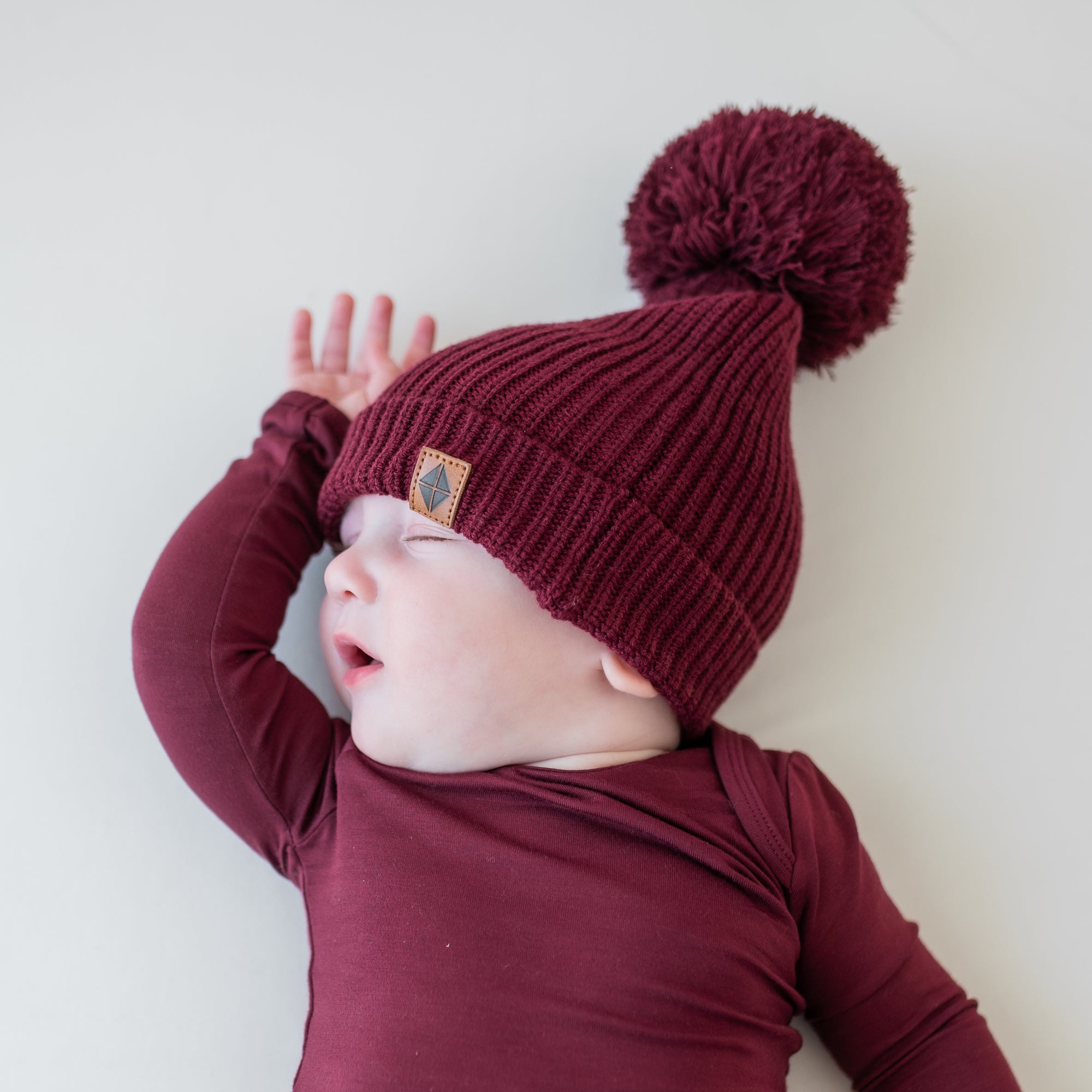 Sleeping infant wearing the Chunky Knit Pom Beanie in Burgundy