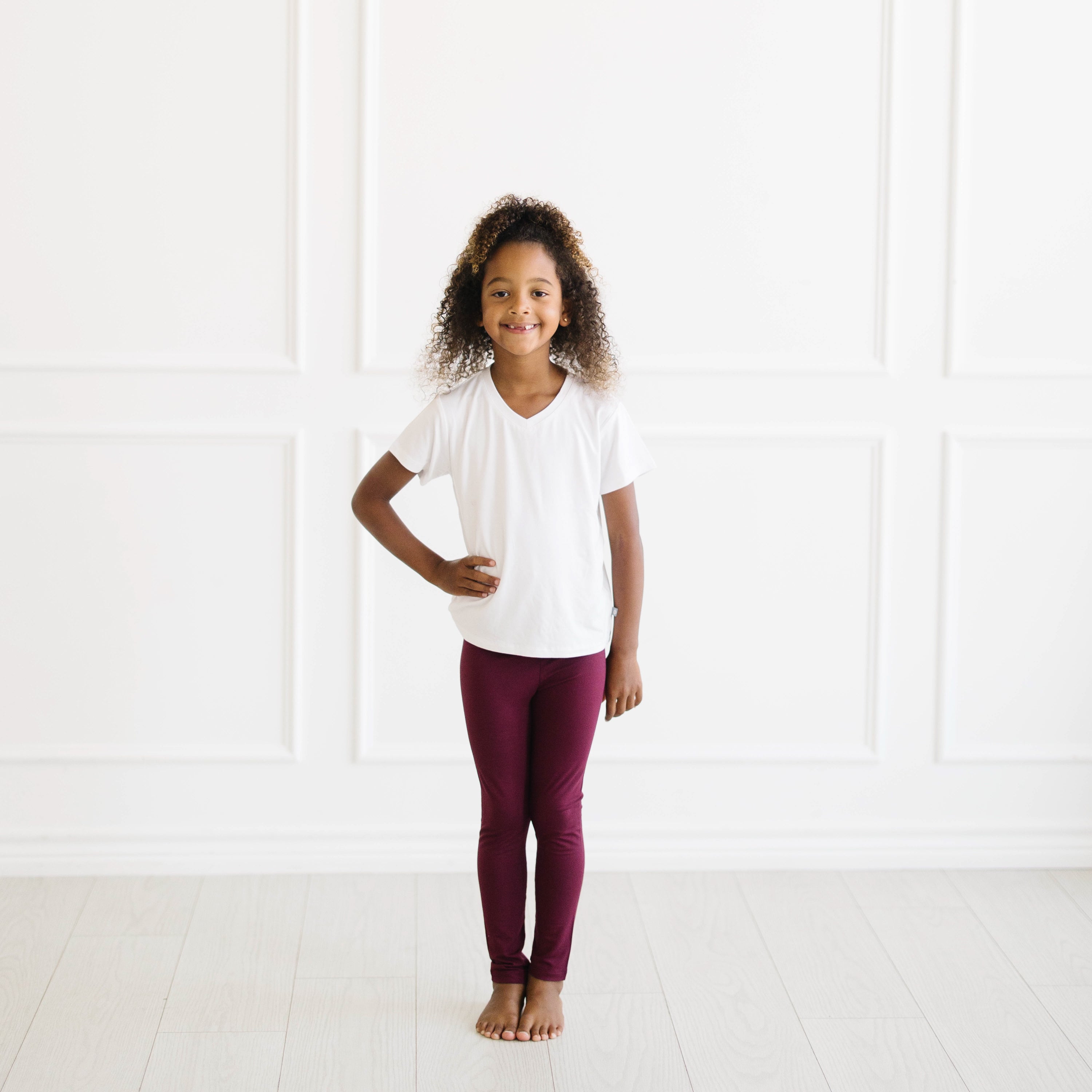 Child standing with one hand on her hip wearing the Toddler Leggings in Burgundy paired with a Snow v-neck