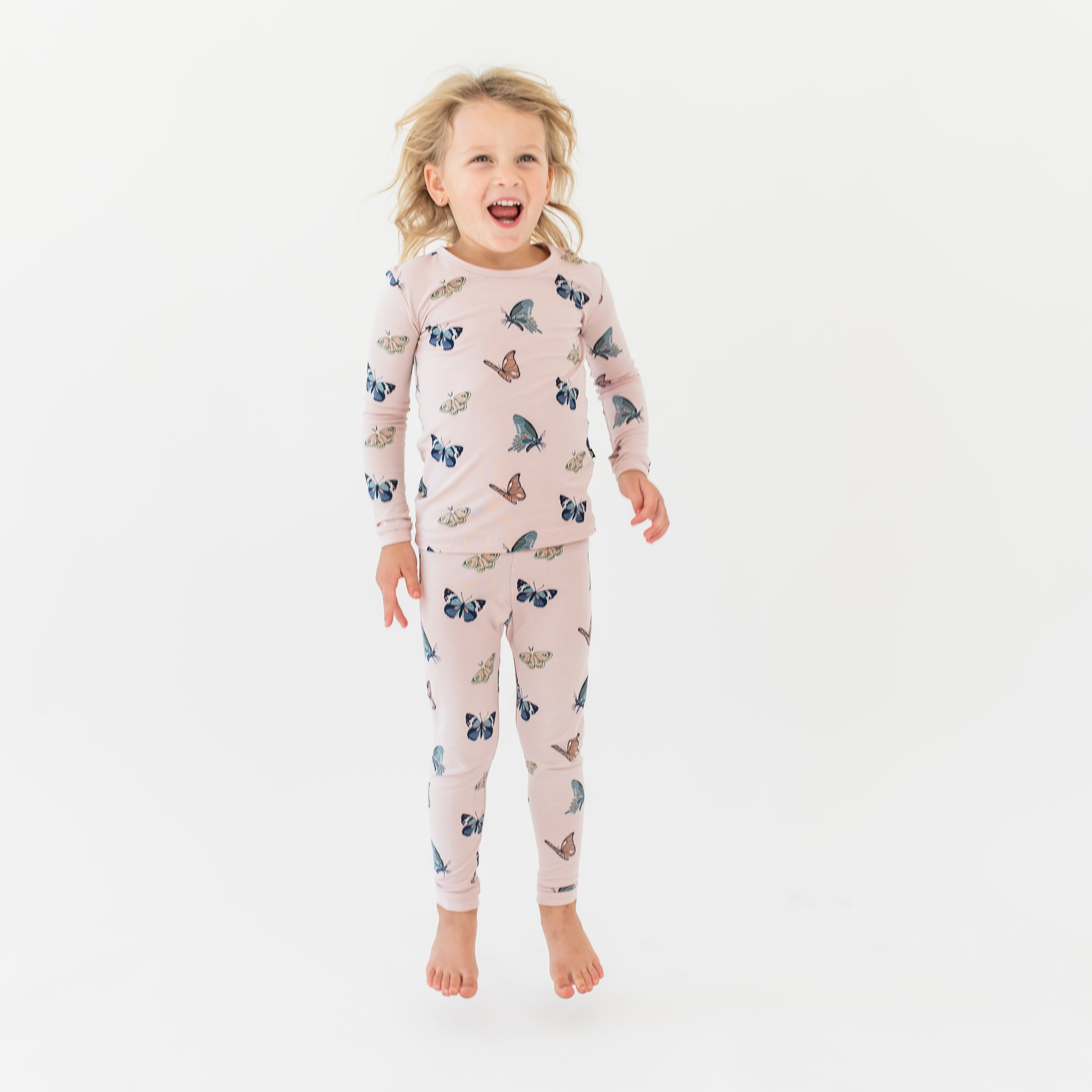 Young girl jumping wearing the Long Sleeve Pajamas in Blush Butterfly in front of a white background