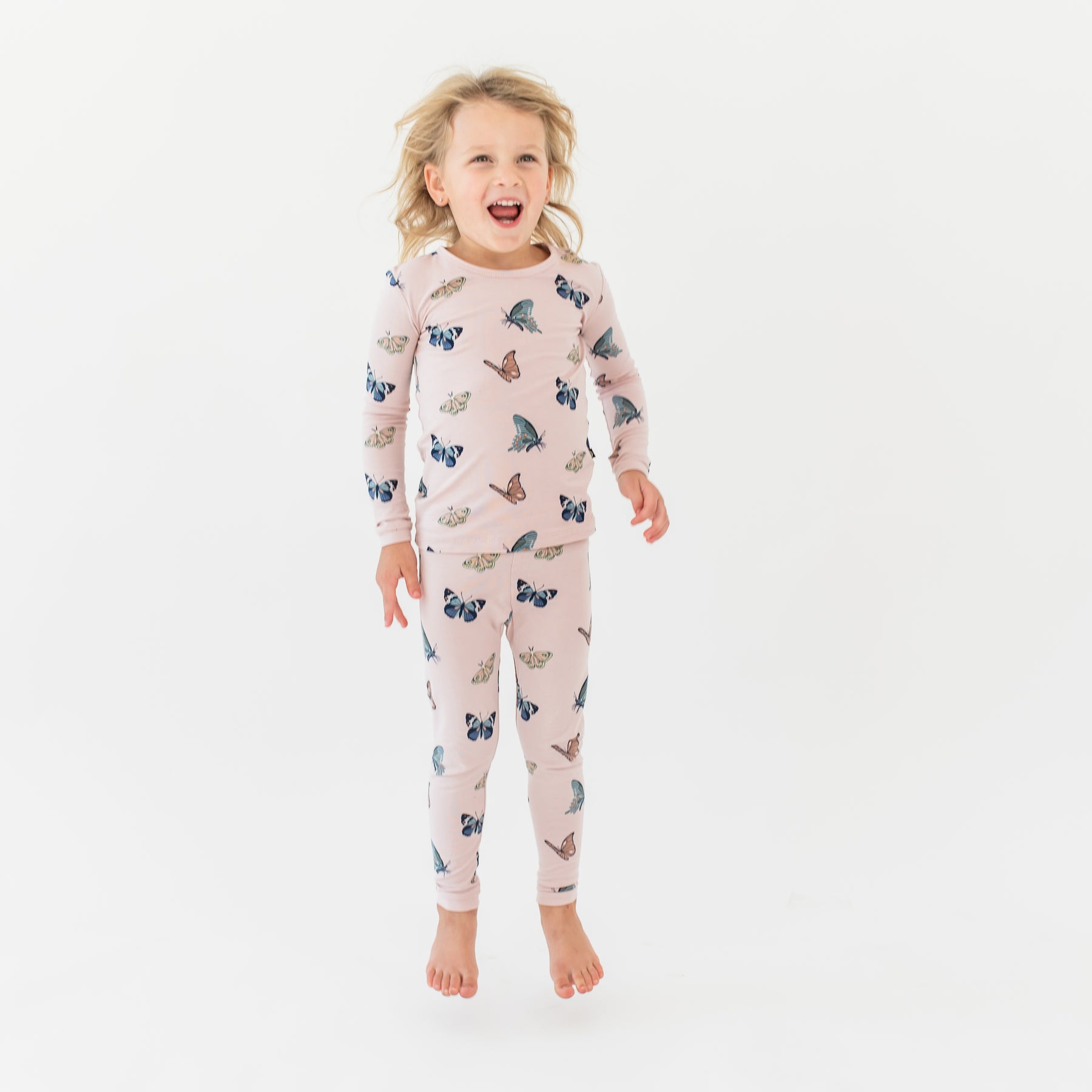 Young girl jumping wearing the Long Sleeve Pajamas in Blush Butterfly in front of a white background