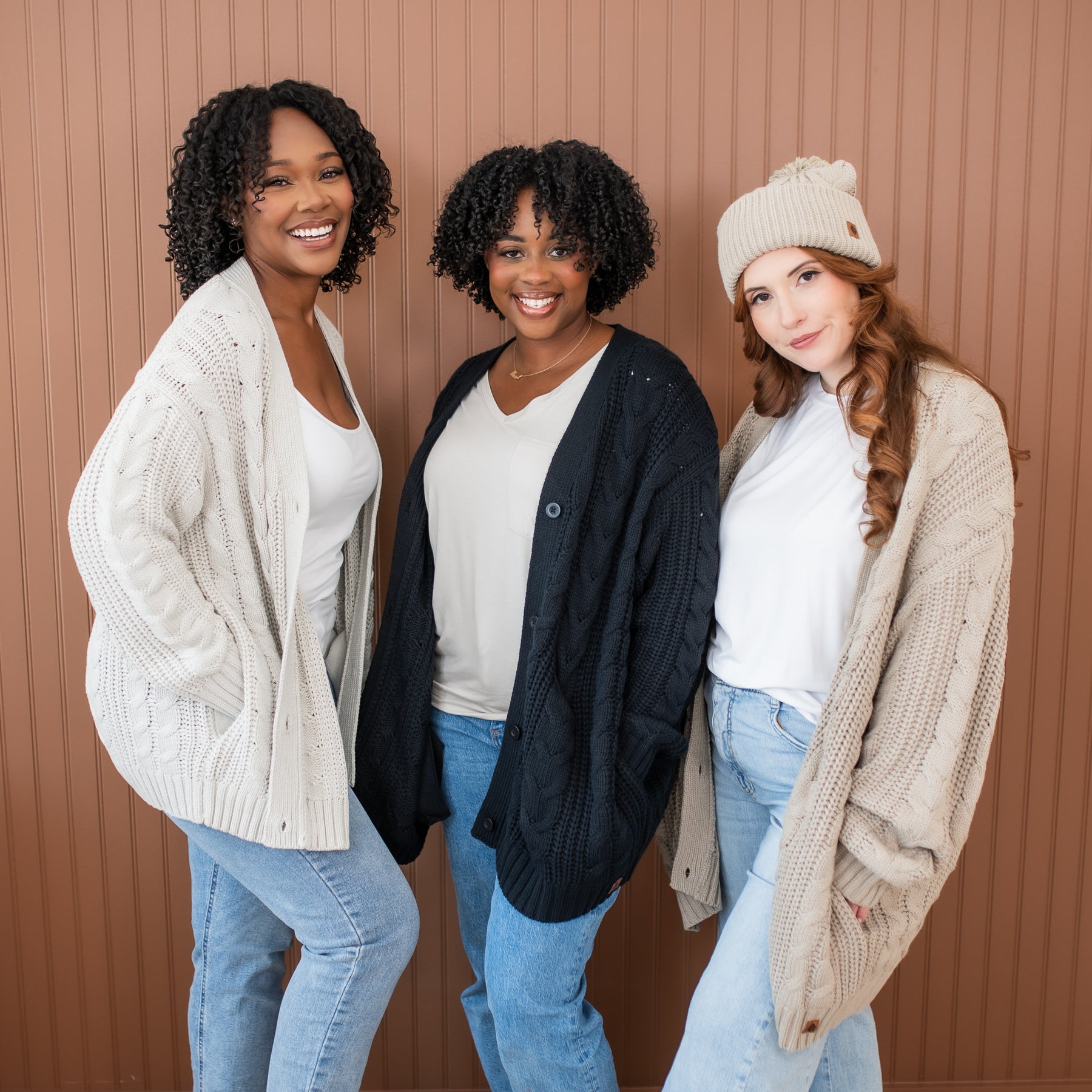 Three female models standing beside one another wearing the Cable Knit Adult Cardigan in Oat, Midnight and Almond