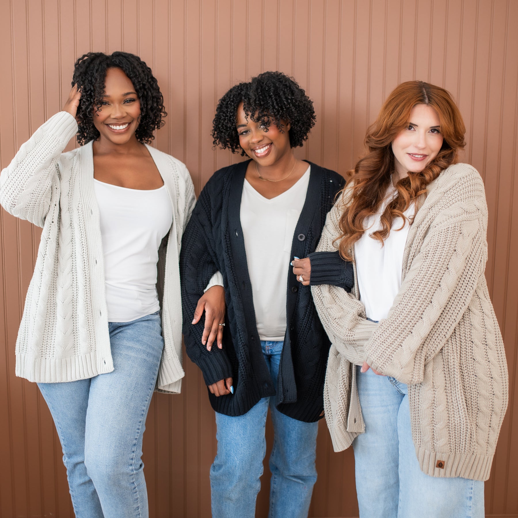 Three female models standing beside one another wearing the Cable Knit Adult Cardigan in Midnight, Oat and Almond