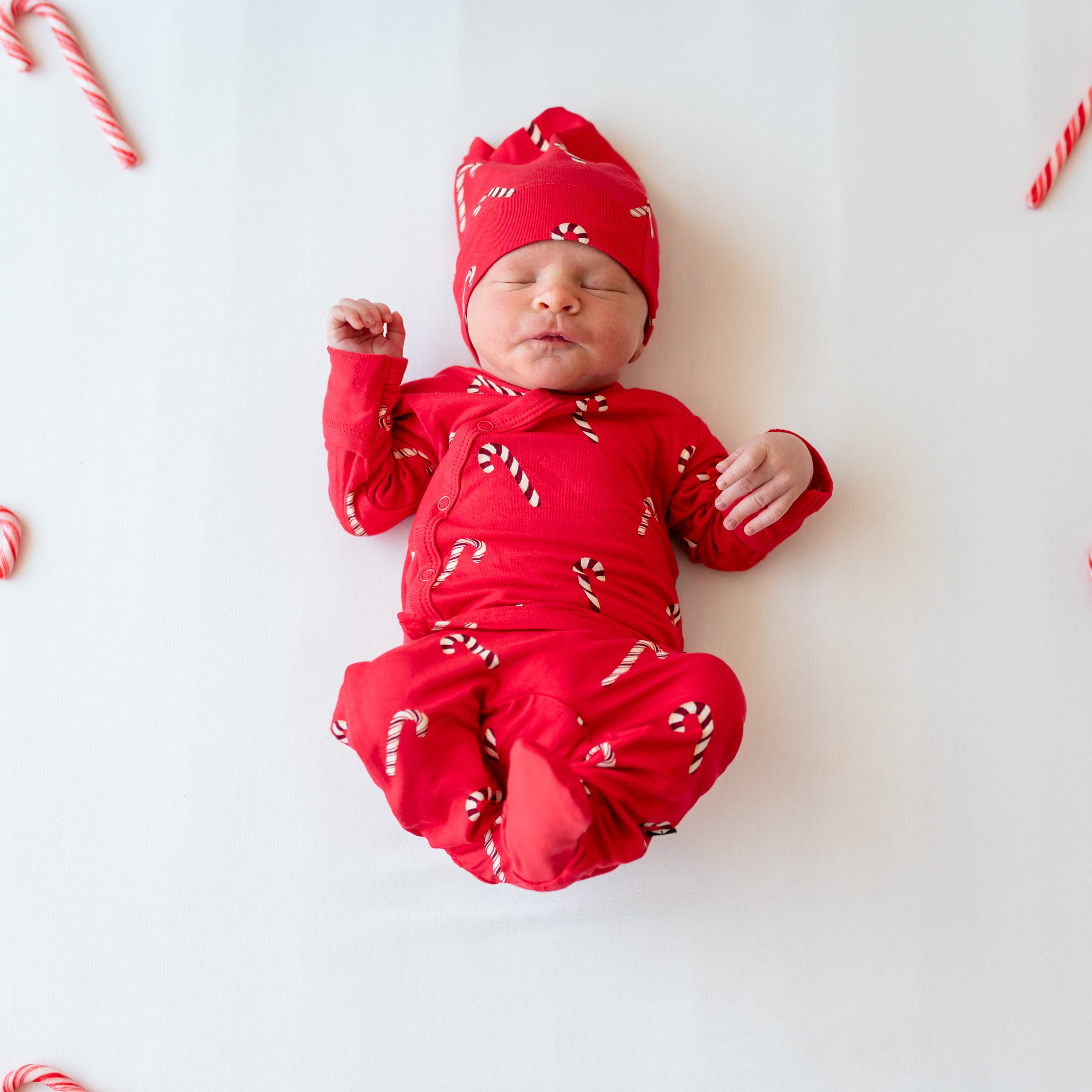 Newborn laying down with their legs in the air wearing the Take Me Home Set with Cap in Candy Cane surrounded by candy canes