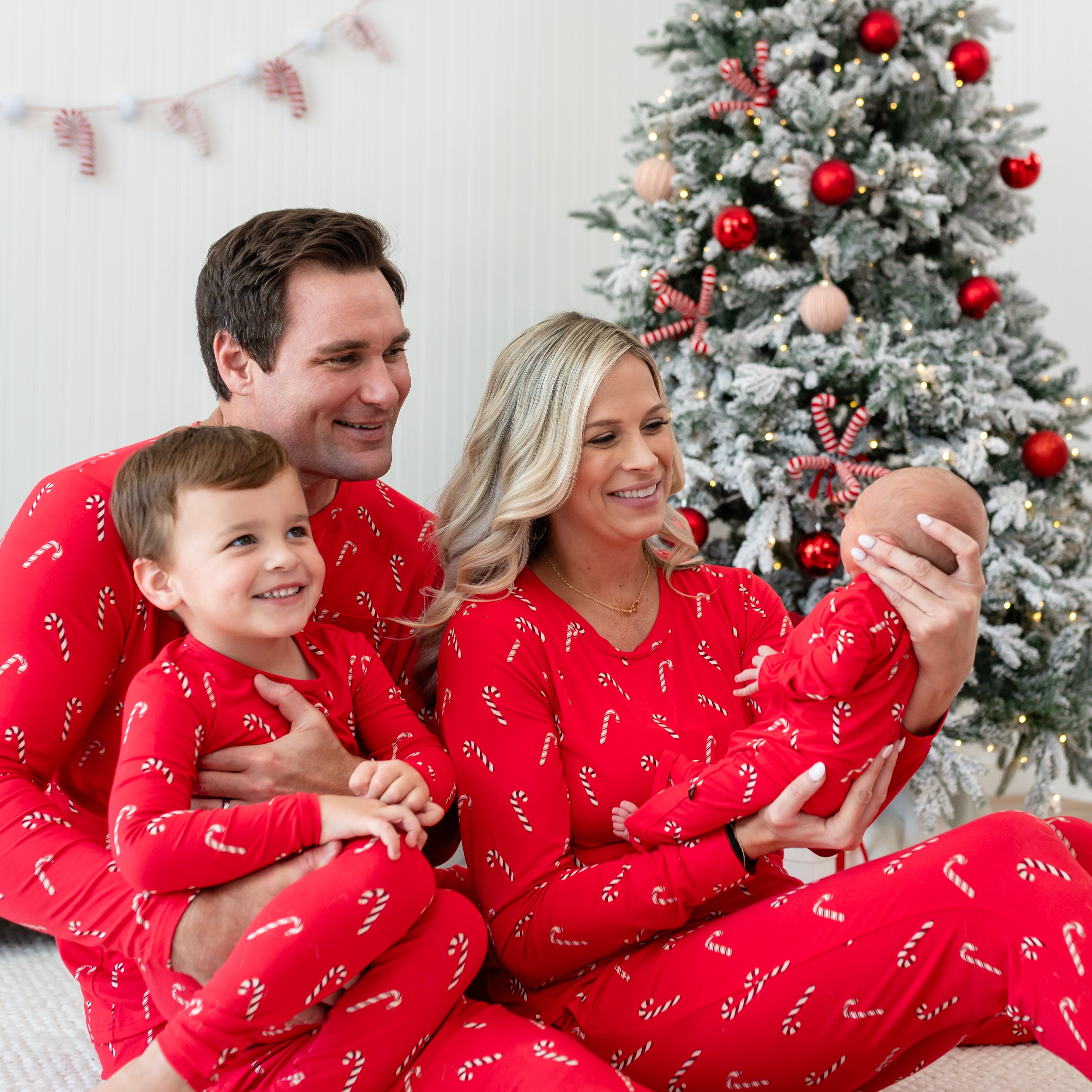 Family of four sitting on an ottoman in front of a decorated Christmas tree matching in the Candy Can holiday print