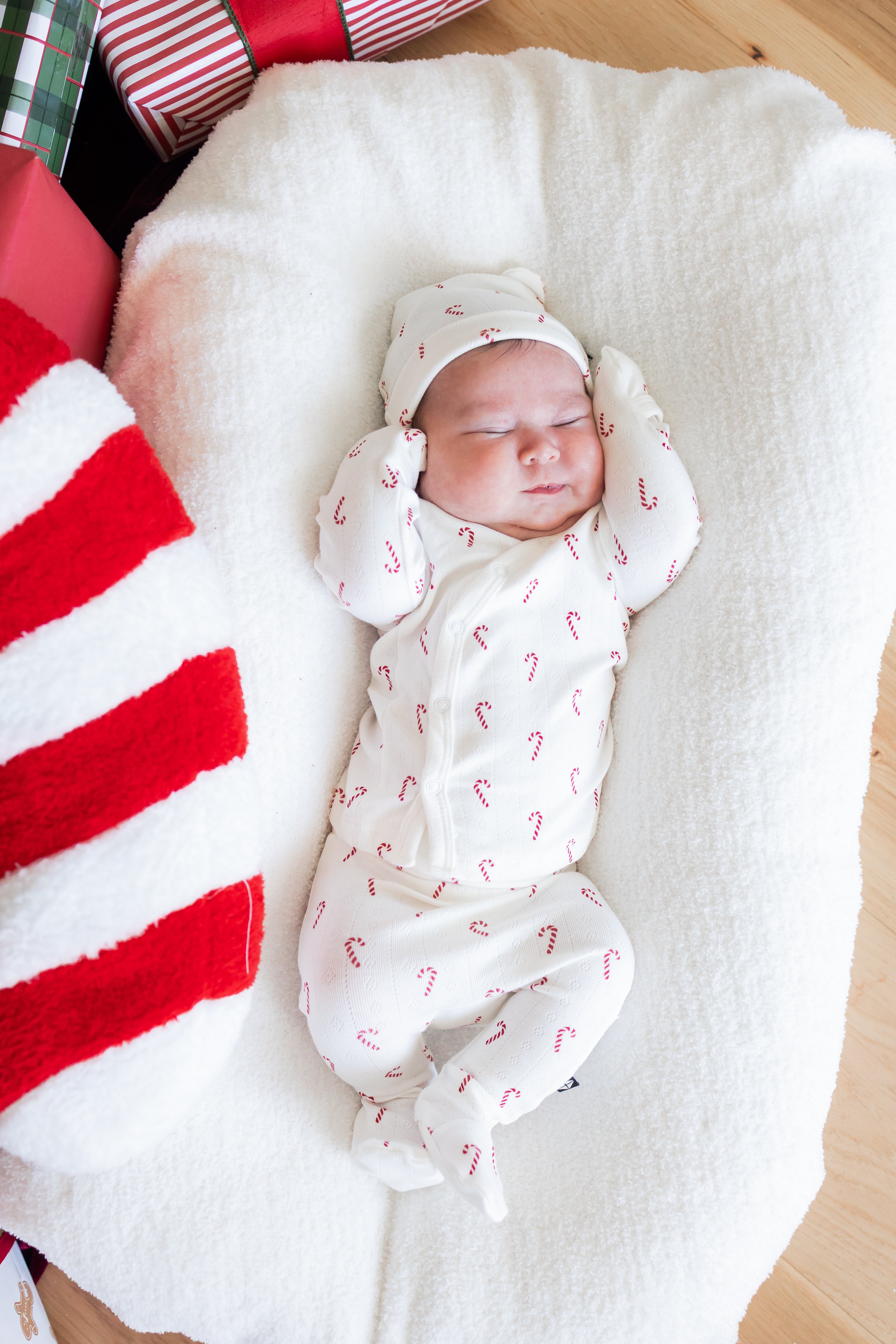 Baby sleeping wearing Pointelle Take Me Home Set with Cap in Candy Cane print on a white crib sheet