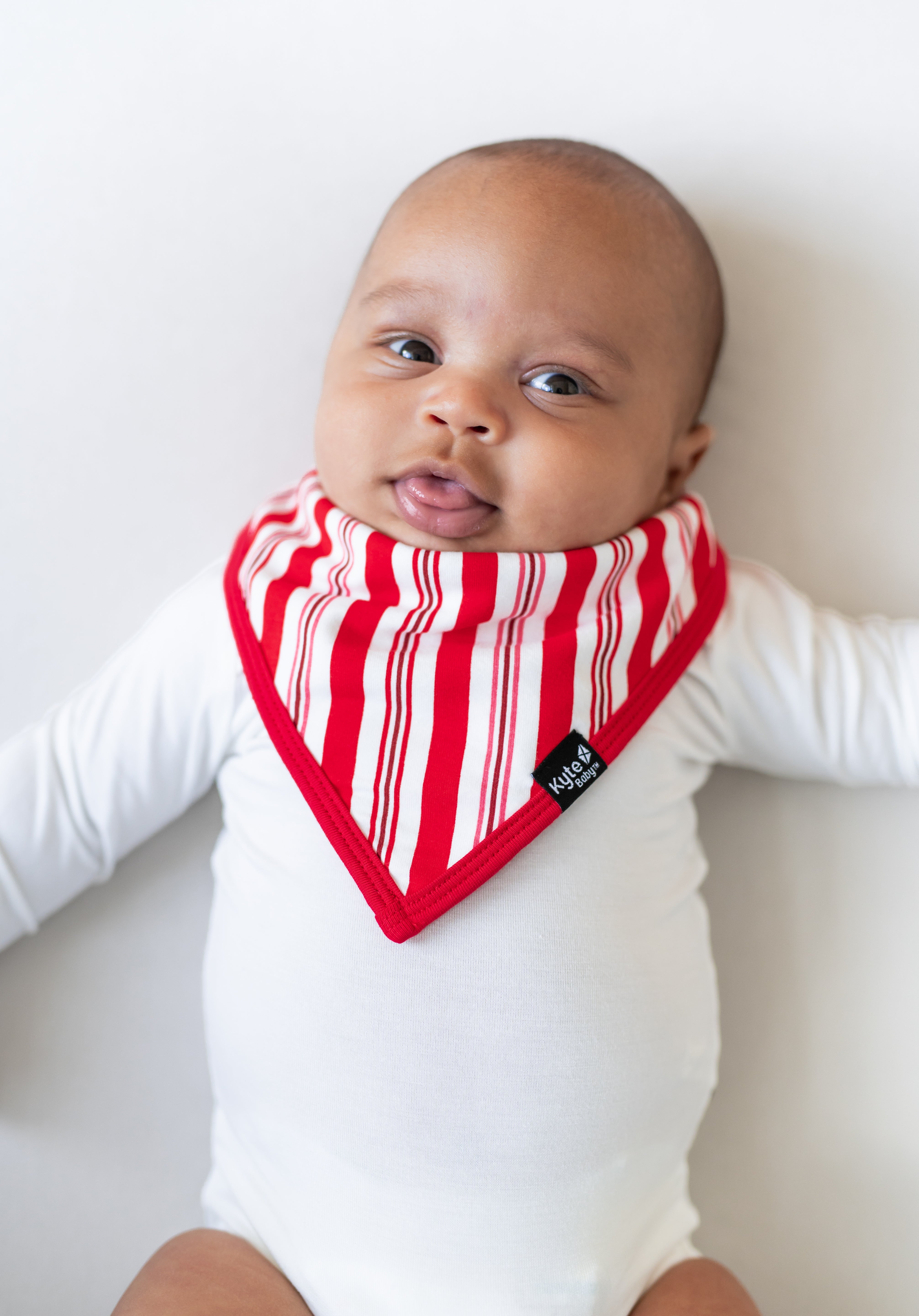 Baby wearing Bib in red and white Peppermint Stripes print over a white bodysuit on a white background
