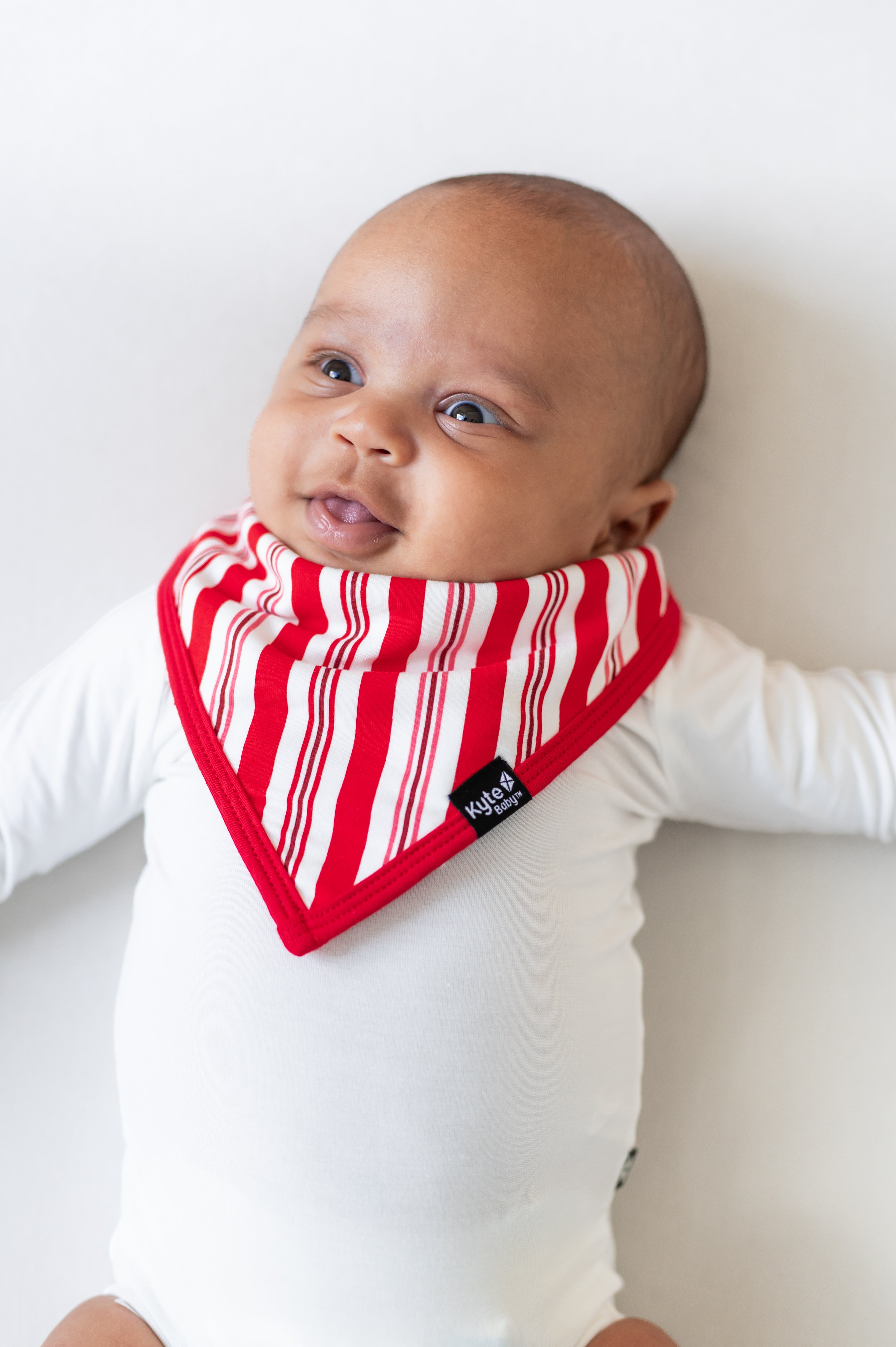 Baby wearing Bib in red and white Peppermint Stripes print over a white bodysuit on a white background