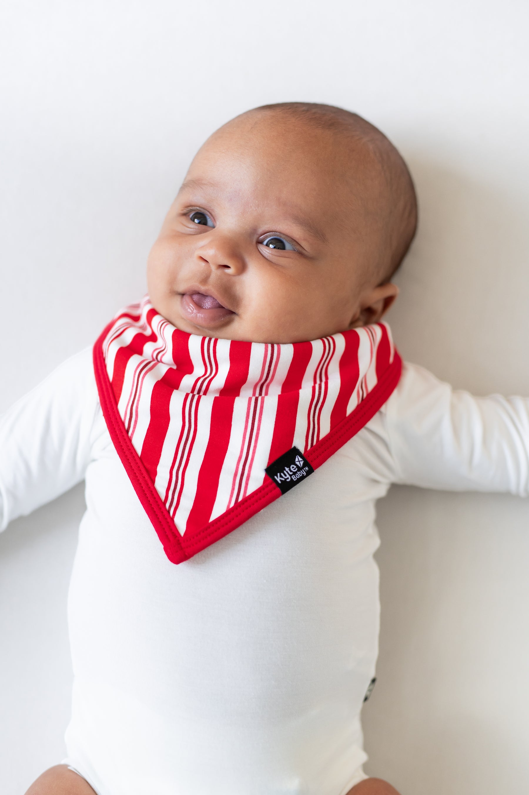 Baby wearing Bib in red and white Peppermint Stripes print over a white bodysuit on a white background