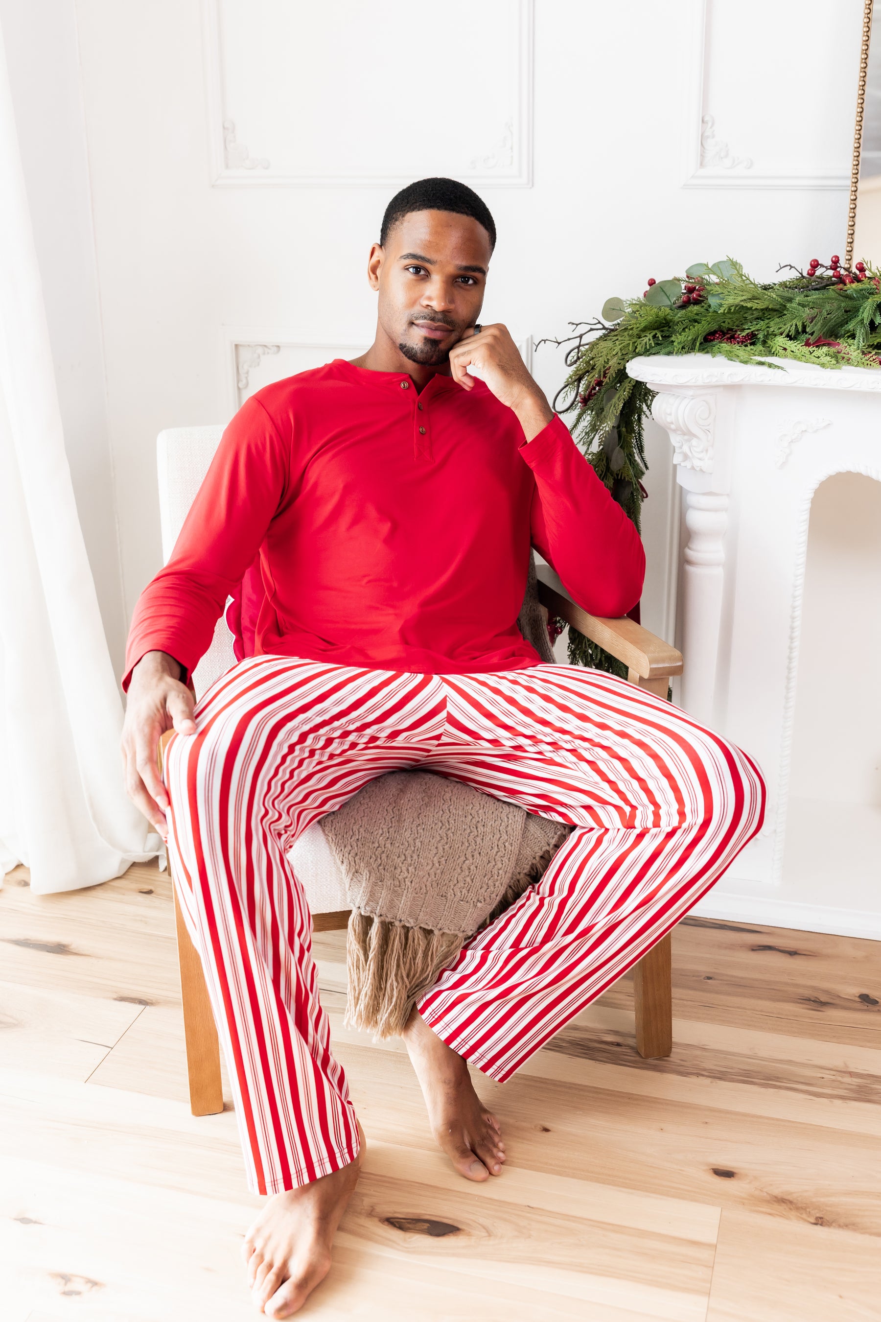 Modal wearing Men's Lounge Pants in red and white Peppermint Stripes print under red T-shirt sitting on a chair