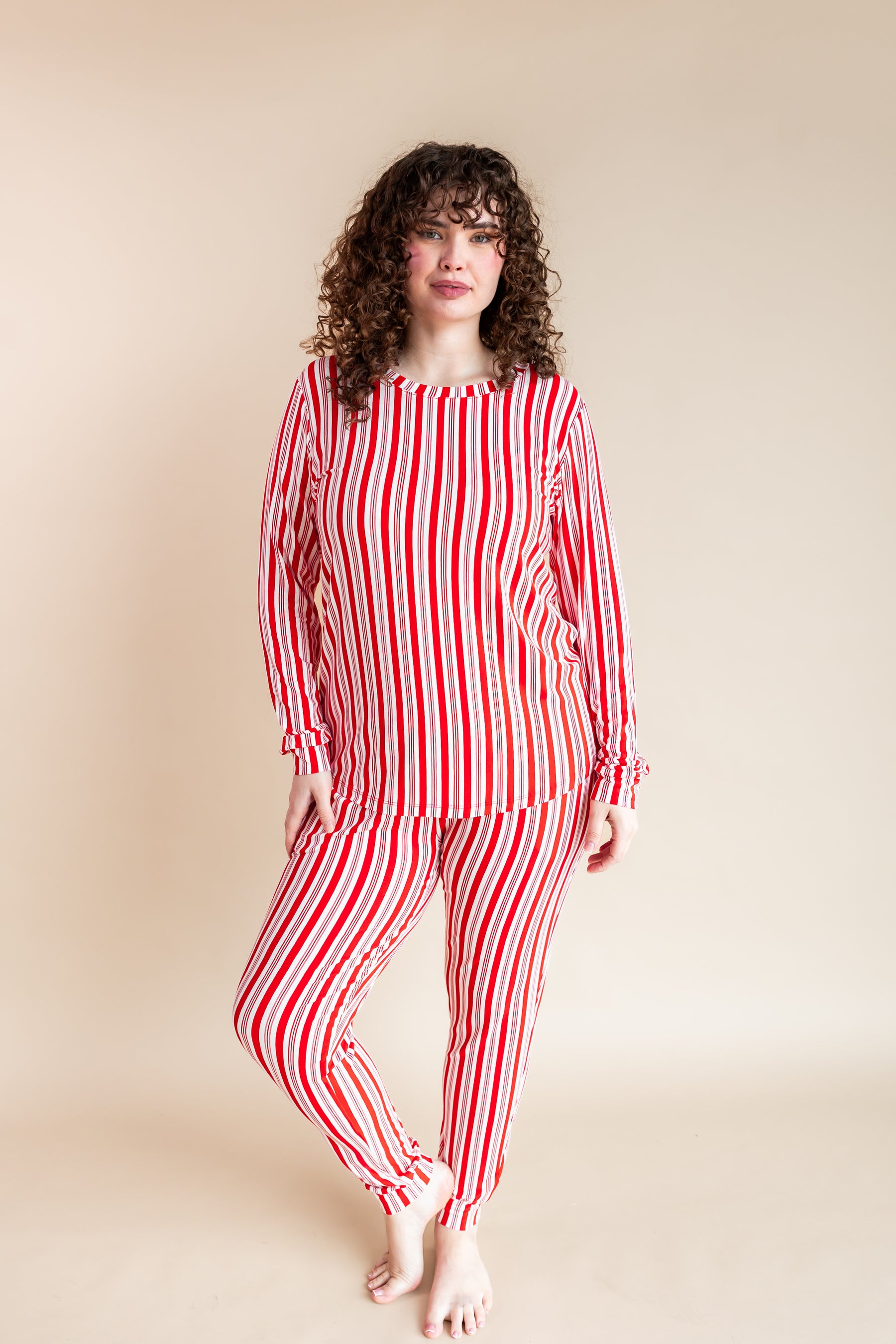 Woman wearing Women's Jogger Pajama Set in red and white Peppermint Stripes print on a beige background